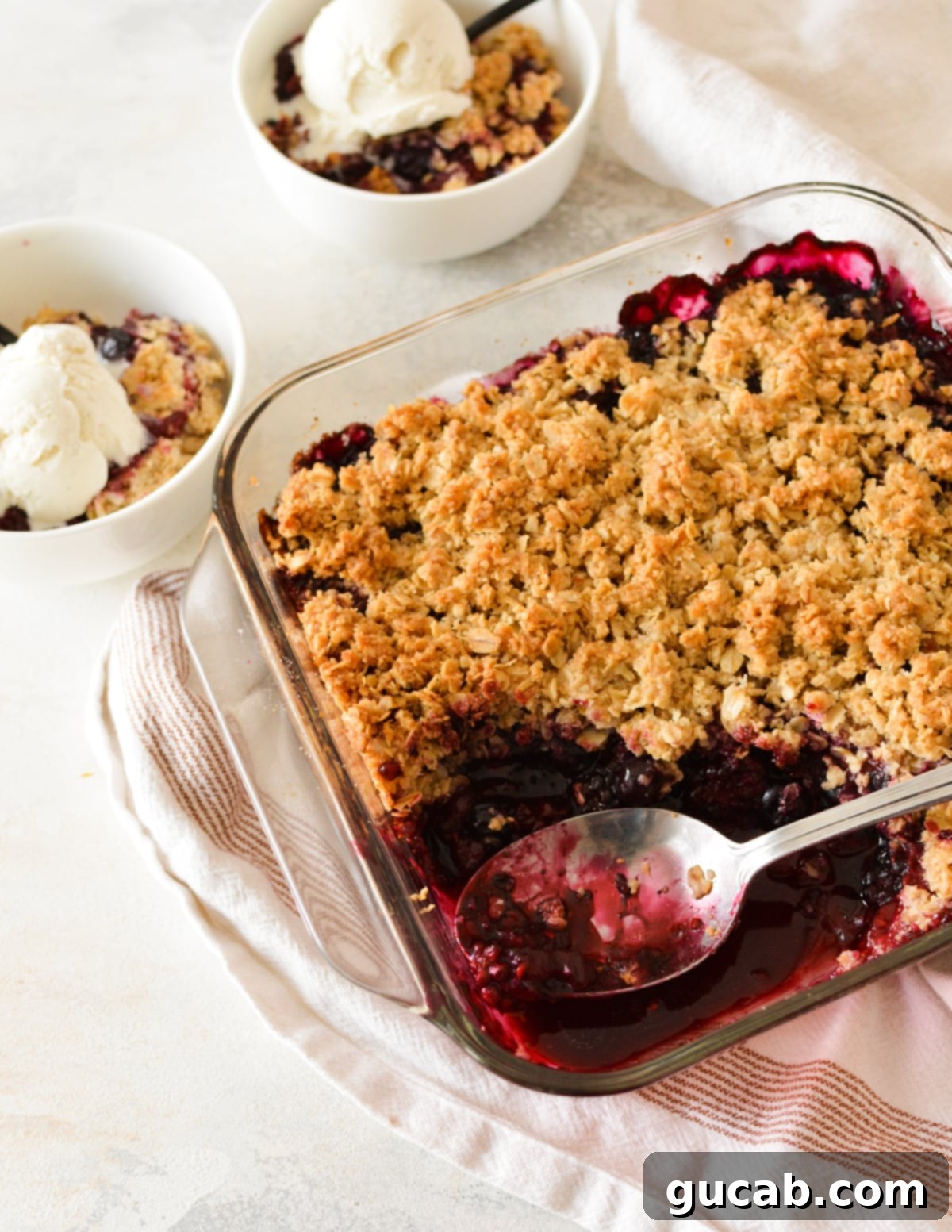 A stunning triple berry crisp, still warm from the oven, with a spoon digging into the bubbling fruit and crispy oat topping.