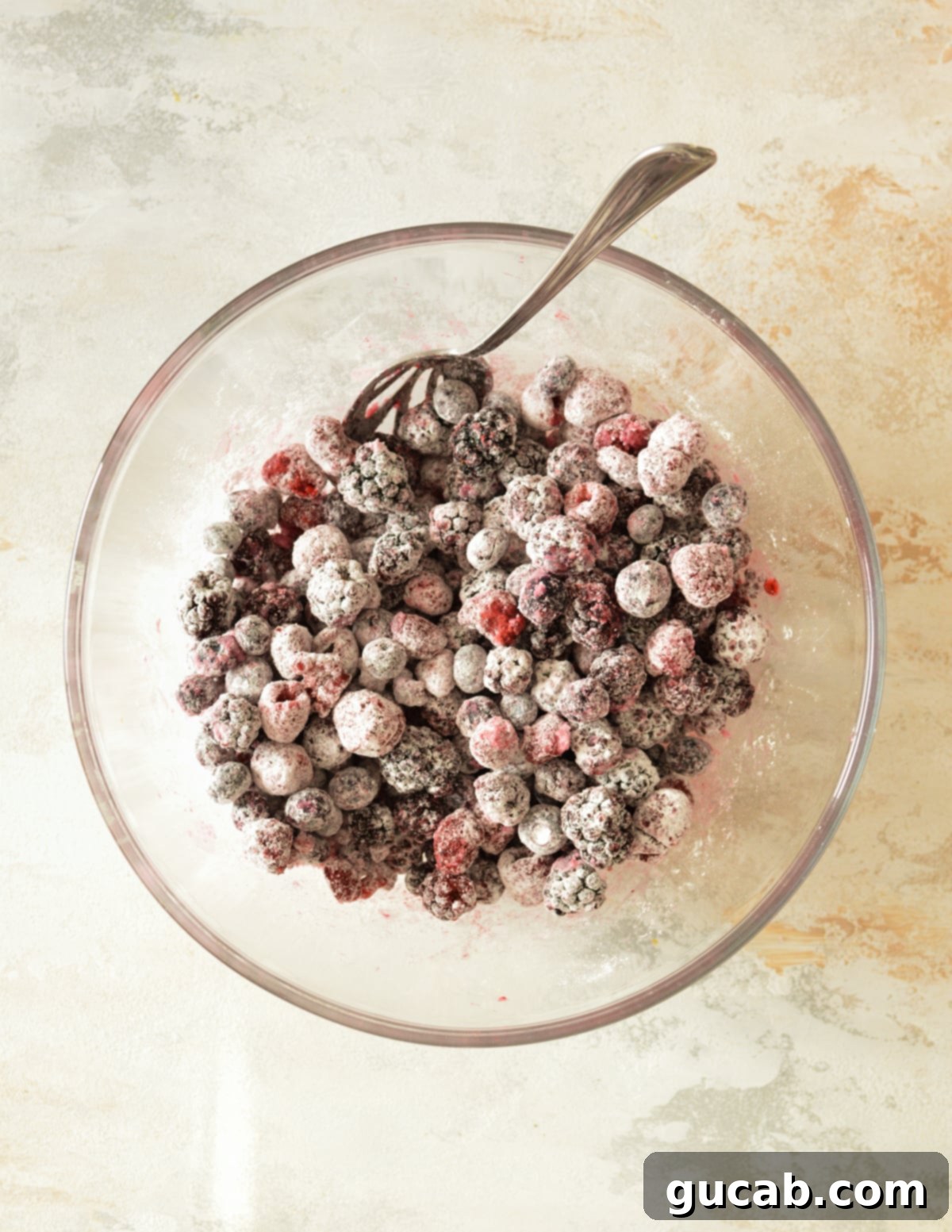 Mixed frozen berries coated evenly with cornstarch, sugar, and lime juice in a bowl.
