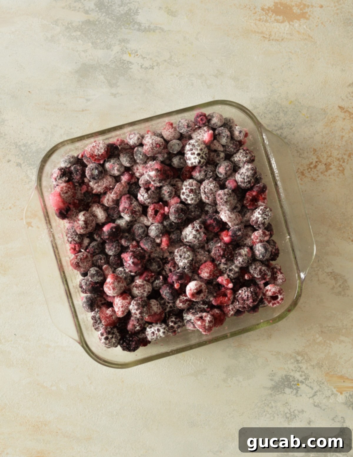 Frozen mixed berries, coated in a sugary lime and cornstarch mixture, nestled in a baking dish, ready for their topping.