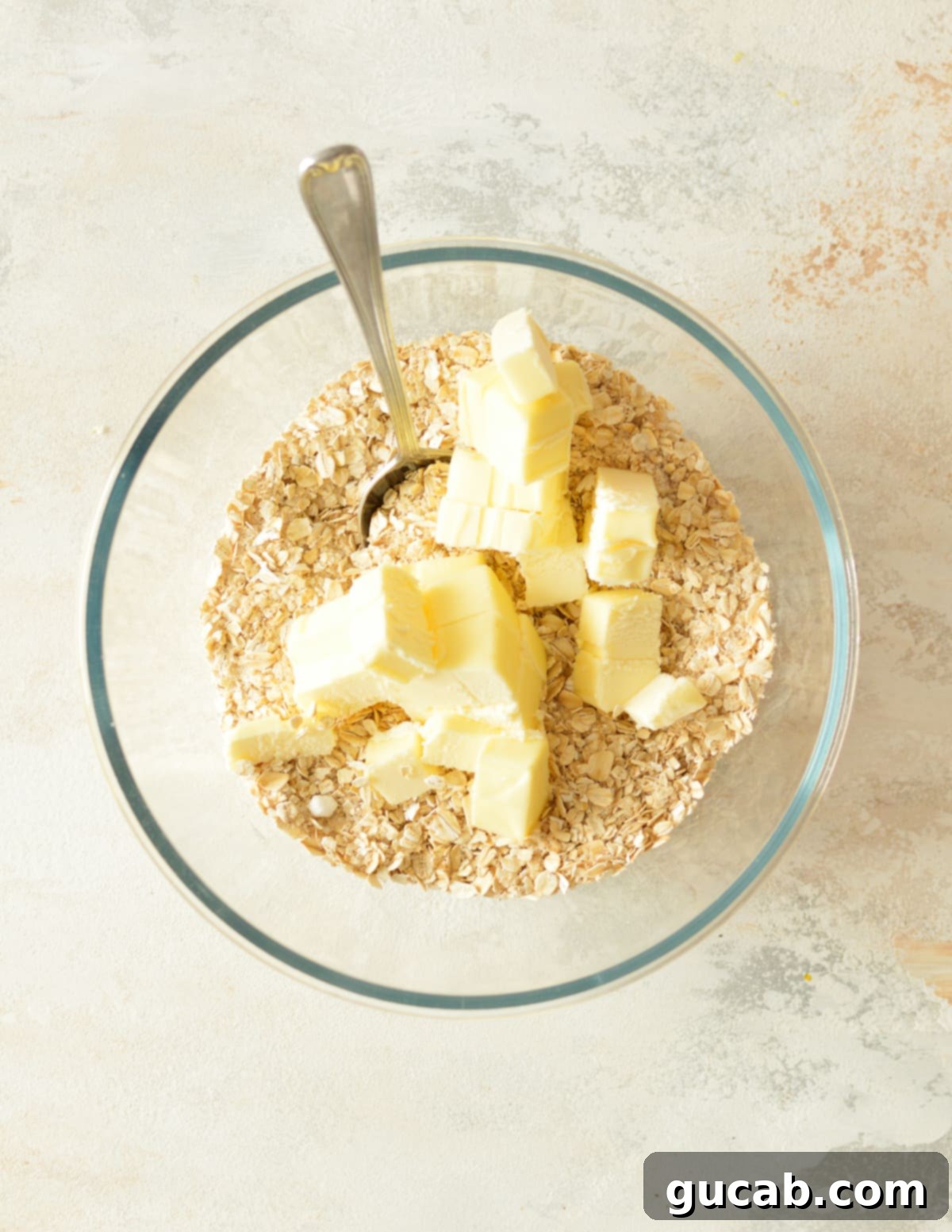 A bowl containing a mixture of oats and sugars, with cold pieces of unsalted butter scattered over the top, ready to be cut in.