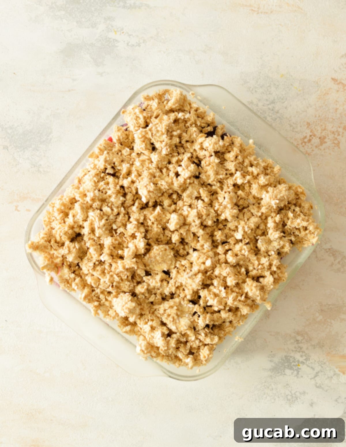 An unbaked mixed berry crisp with a generous, even layer of golden oat crumb topping, ready to be put in the oven.