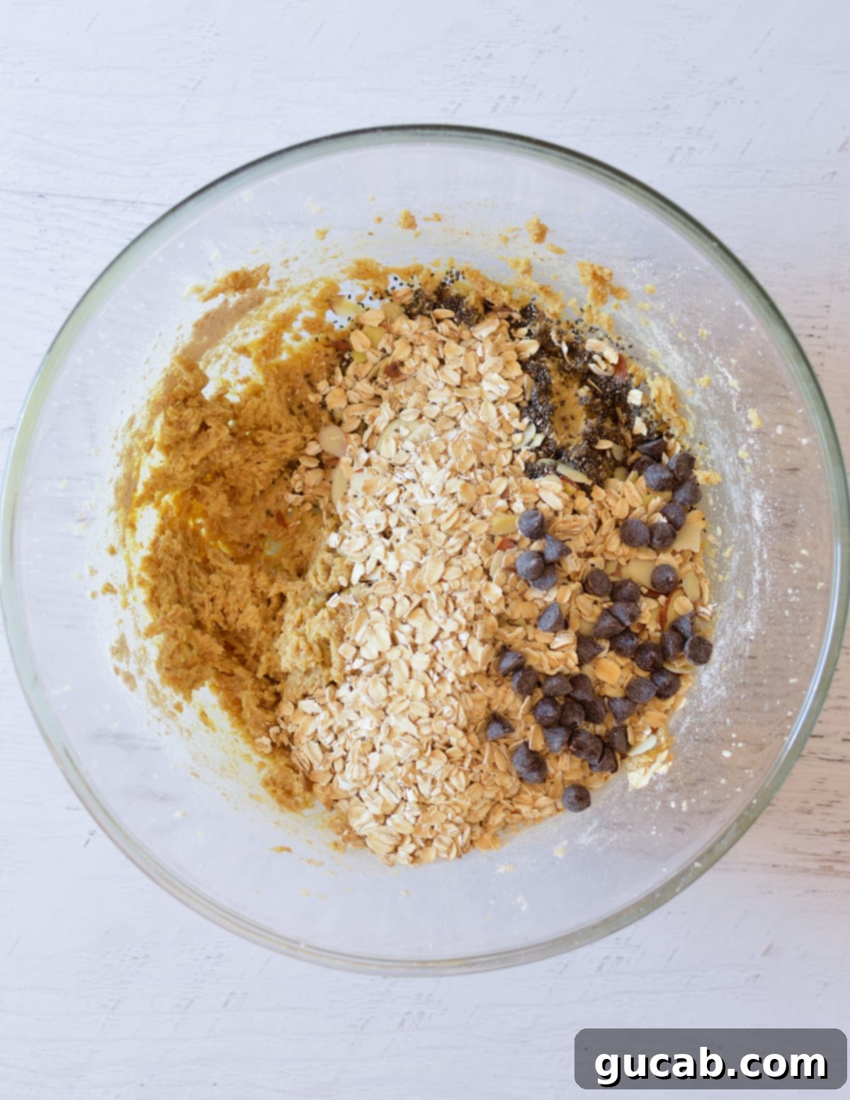 Rolled oats, chia seeds, and chocolate chips layered on top of the cookie dough, ready to be mixed in.