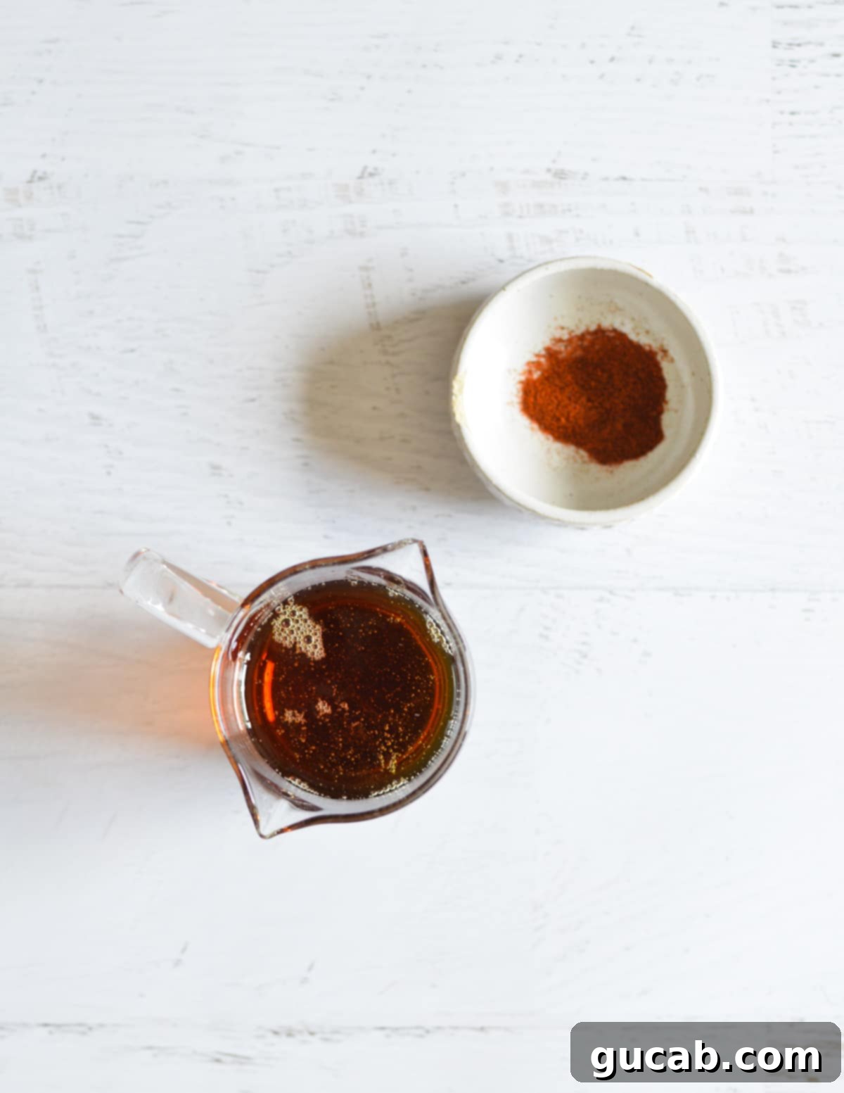 A small bowl of vibrant red cayenne pepper and a glass bottle of pure maple syrup, the two key ingredients.