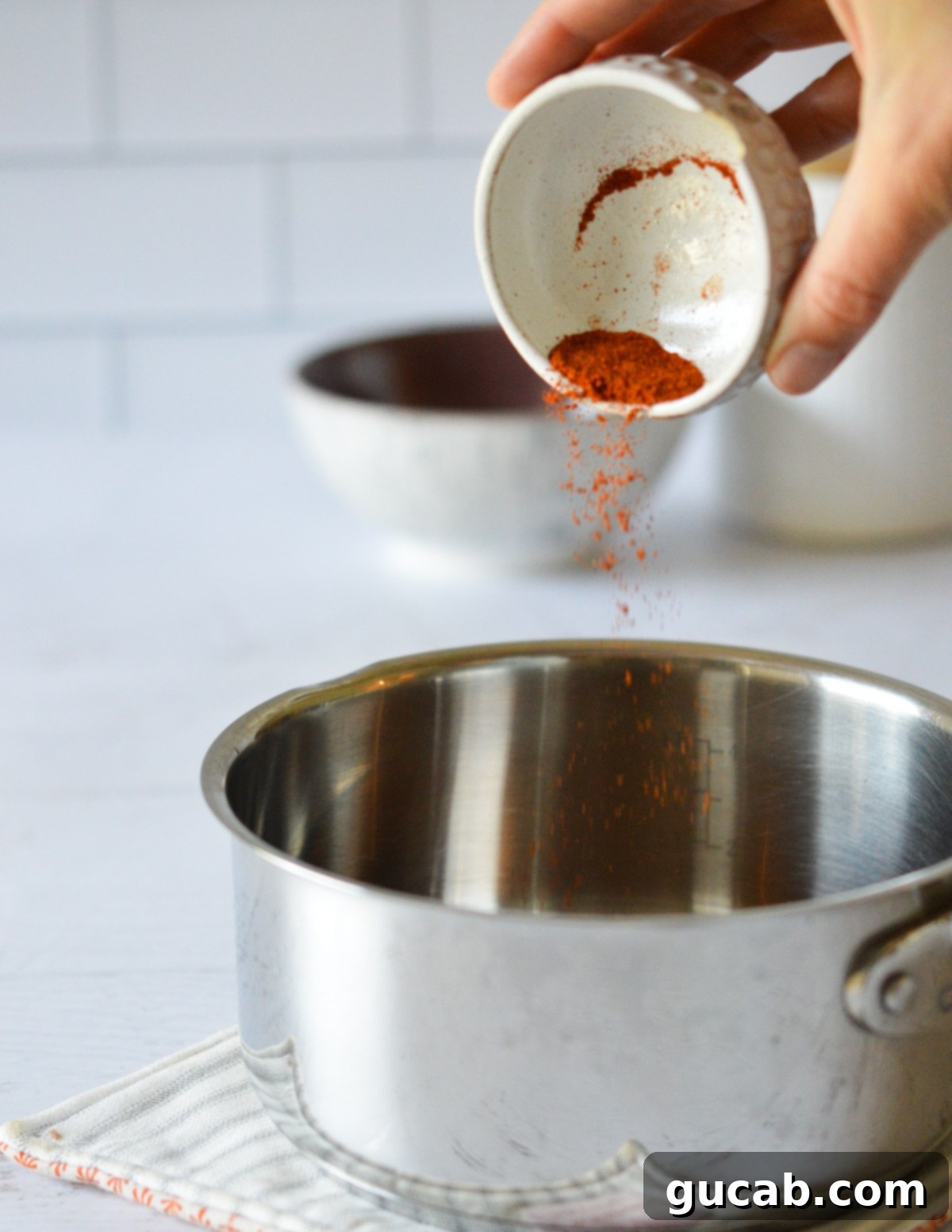 Bright red cayenne pepper being sprinkled into a saucepan filled with golden maple syrup.