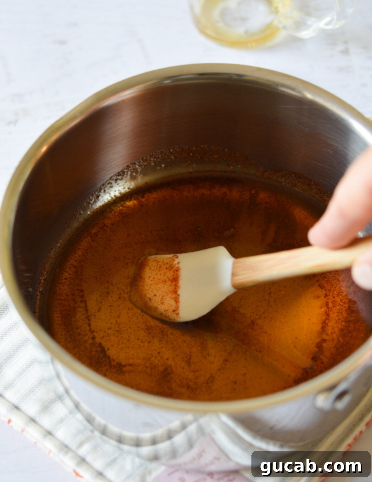 A wooden spatula stirring the simmering blend of maple syrup and cayenne pepper in a saucepan.