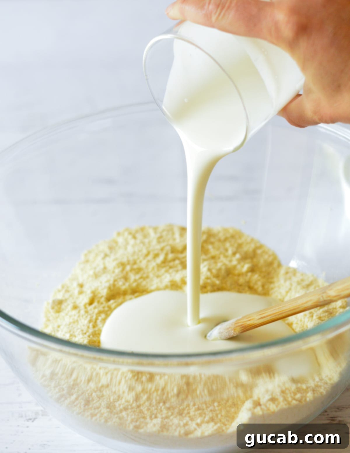 hand pouring buttermilk into a bowl with cornmeal