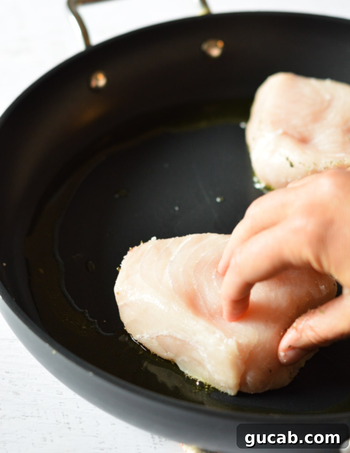 hand placing swordfish into skillet. 