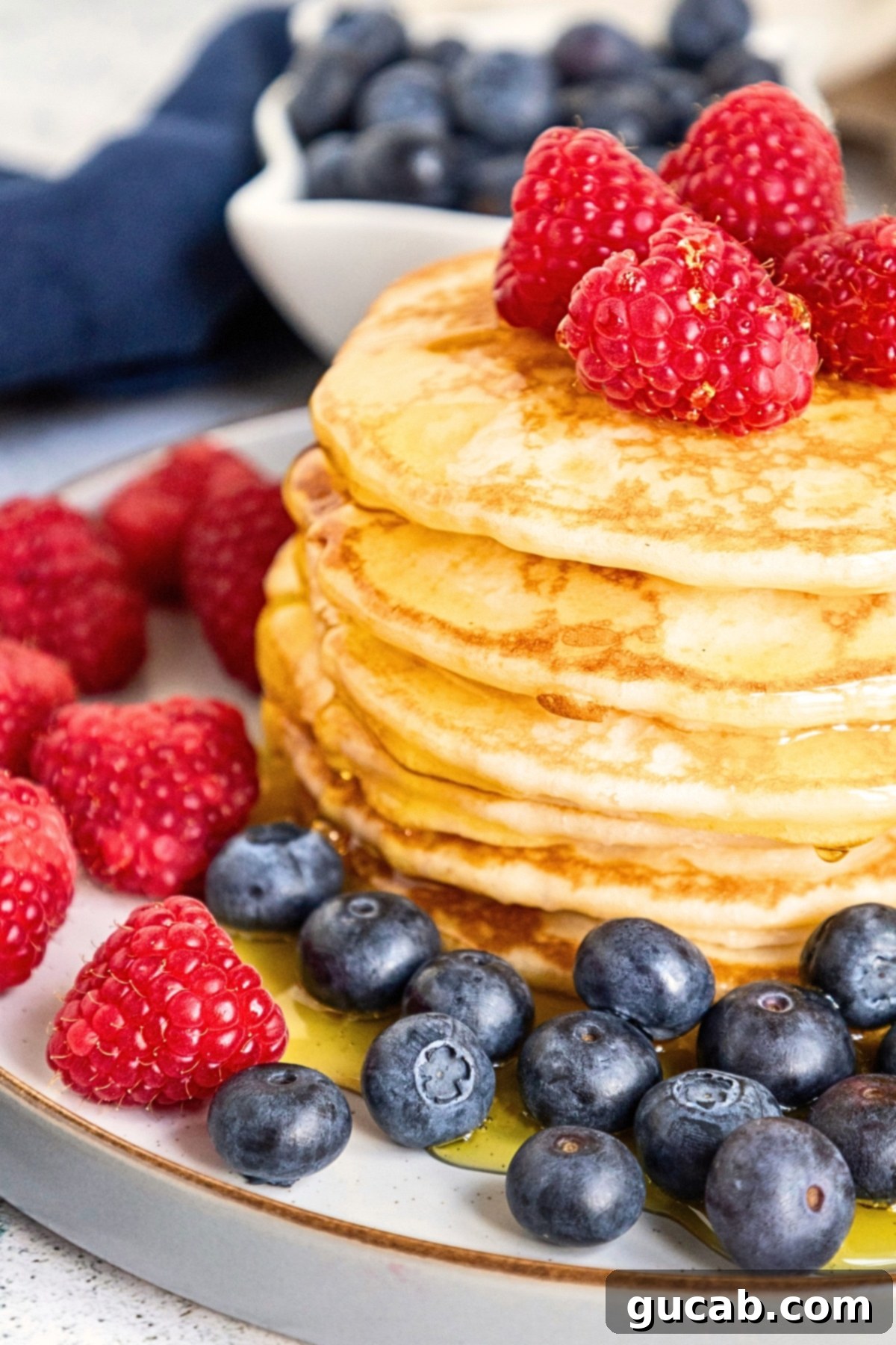 A stack of fluffy gluten-free buttermilk pancakes topped with fresh raspberries and maple syrup.
