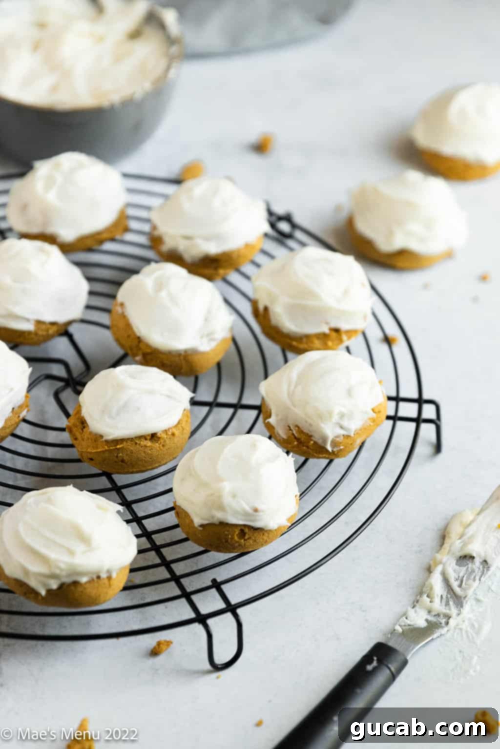 Soft gluten-free pumpkin cookies with creamy icing on a wire rack.