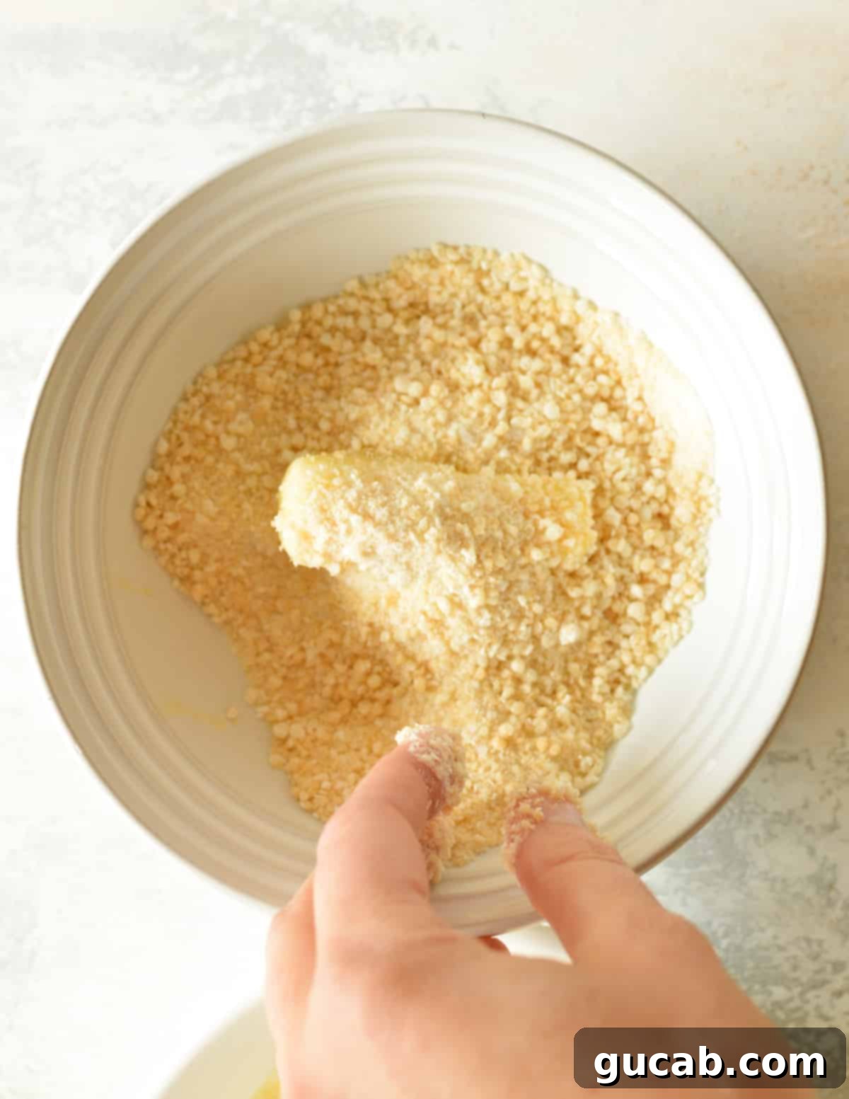 Irresistible Gluten-Free Mozzarella Sticks 7 a cheese stick in a bowl of gluten free breadcrumbs
