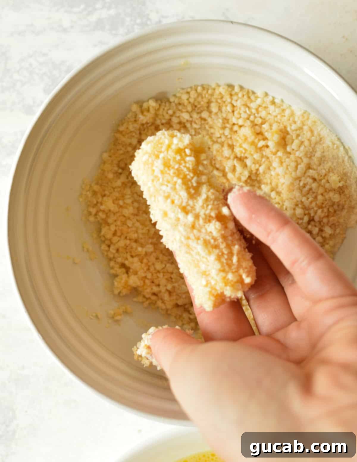 Irresistible Gluten-Free Mozzarella Sticks 9 hand holding a cheese stick coated in gluten free breadcrumbs