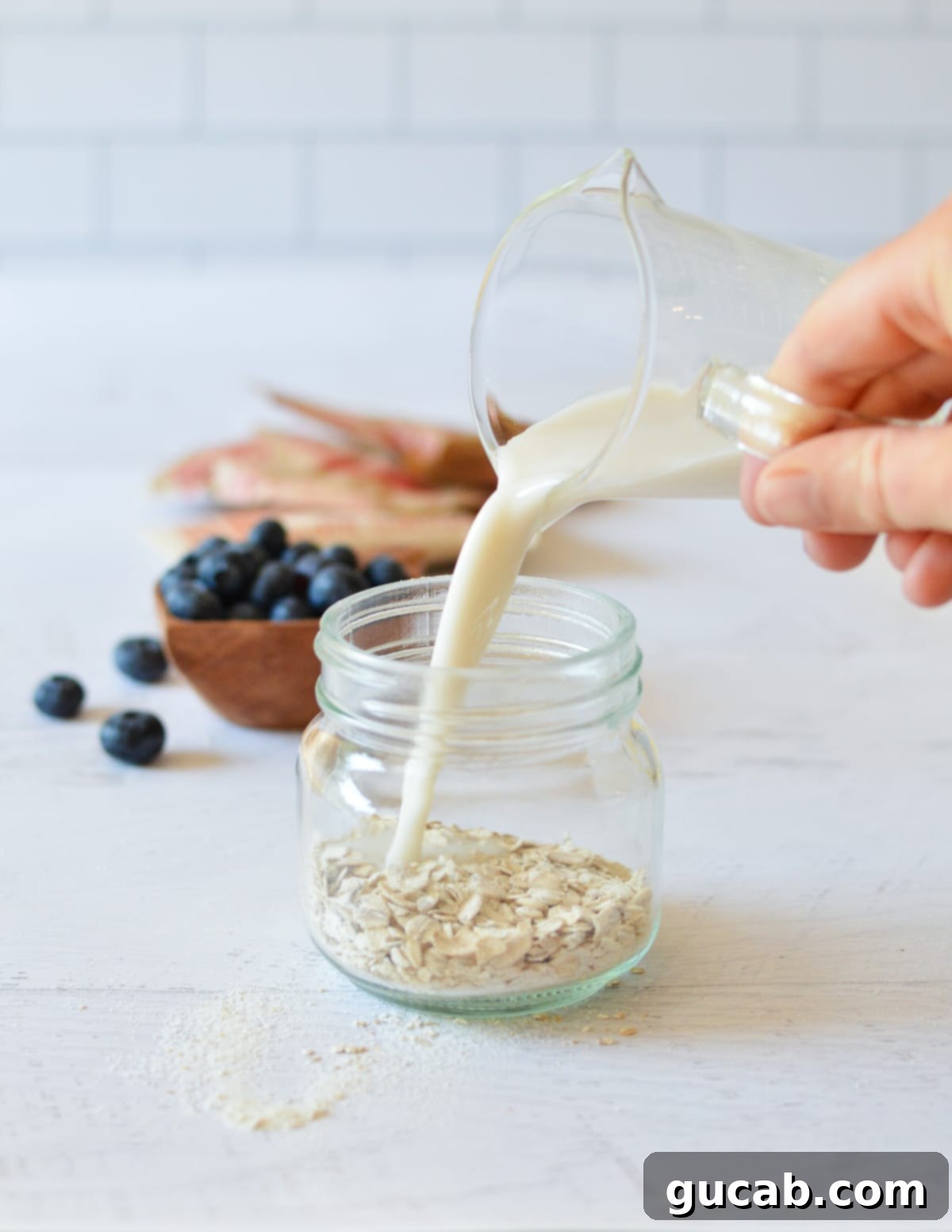 A steady hand pouring milk from a carton into a jar, gently covering the instant oats already inside, ready for stirring.