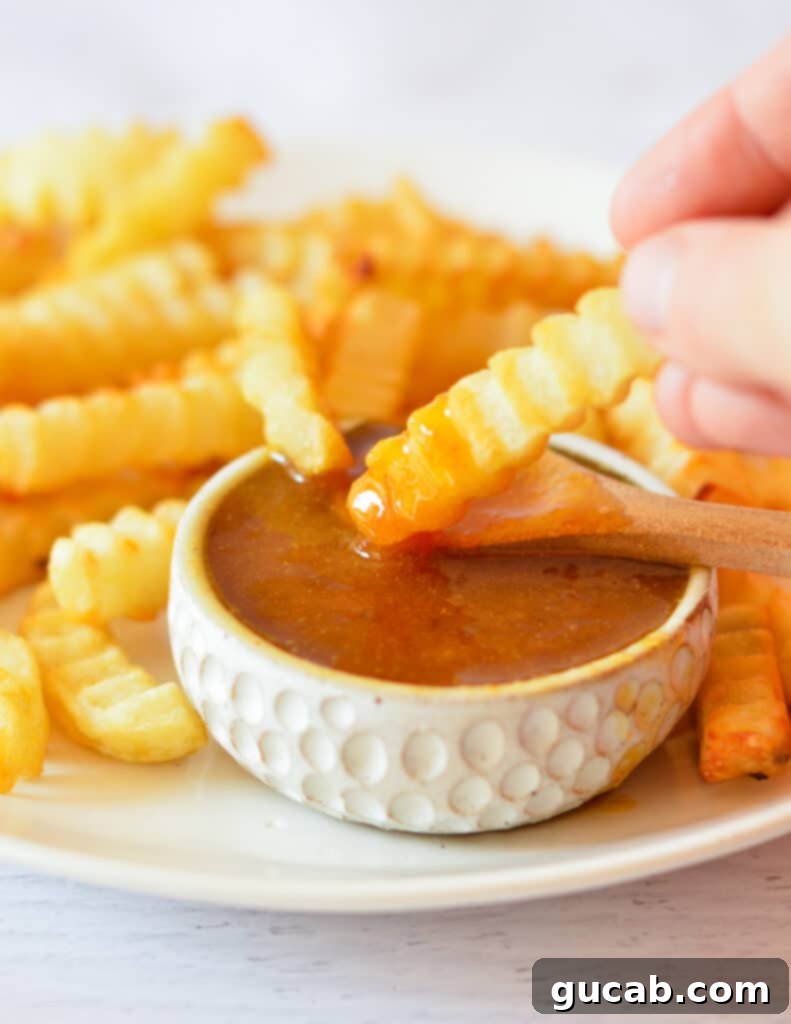 Dipping a golden french fry into a bowl of homemade sweet and sour sauce, showcasing its vibrant orange color and smooth texture.