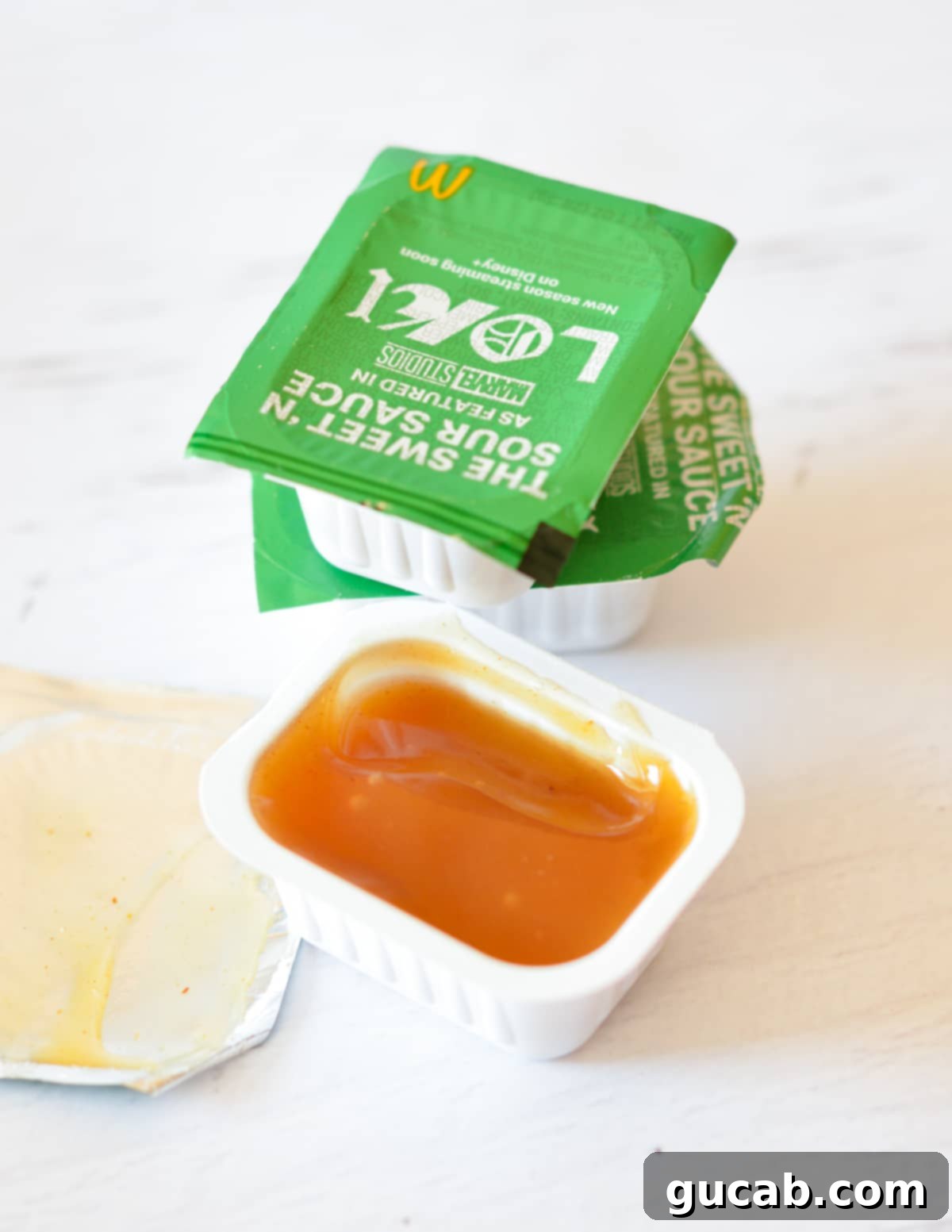 Several McDonald's sweet and sour sauce packets arranged next to a bowl of homemade sweet and sour sauce for comparison.