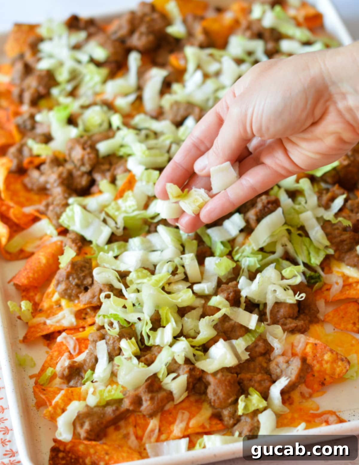 A hand adding shredded lettuce to freshly baked nachos with beef and melted cheese.