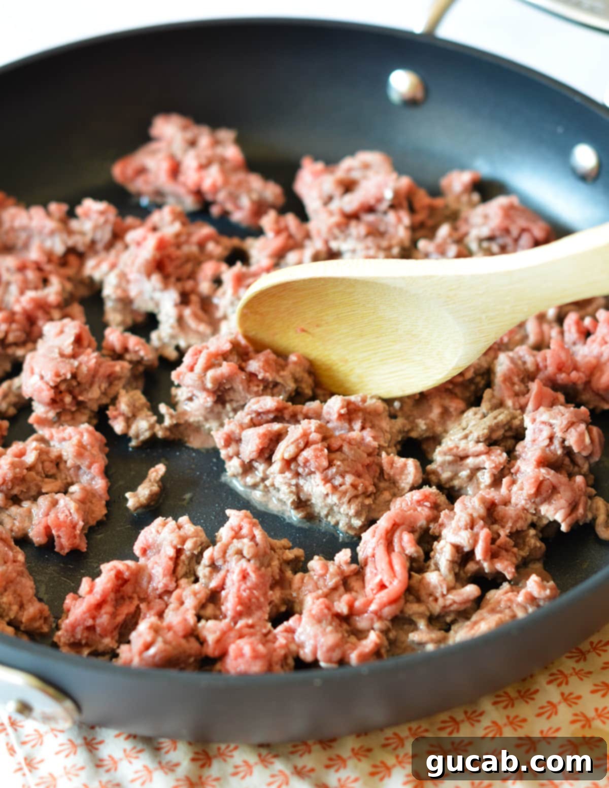 Ground beef browning in a hot skillet, being broken up with a spatula.