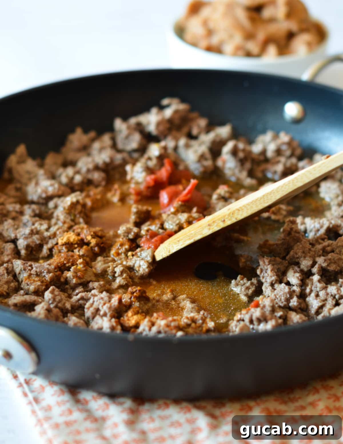 Ground beef, taco seasoning, tomato paste, and water being mixed in a skillet with a spatula.