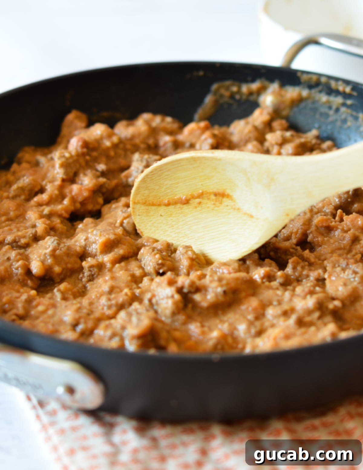 Refried beans being stirred into seasoned ground beef in a skillet.