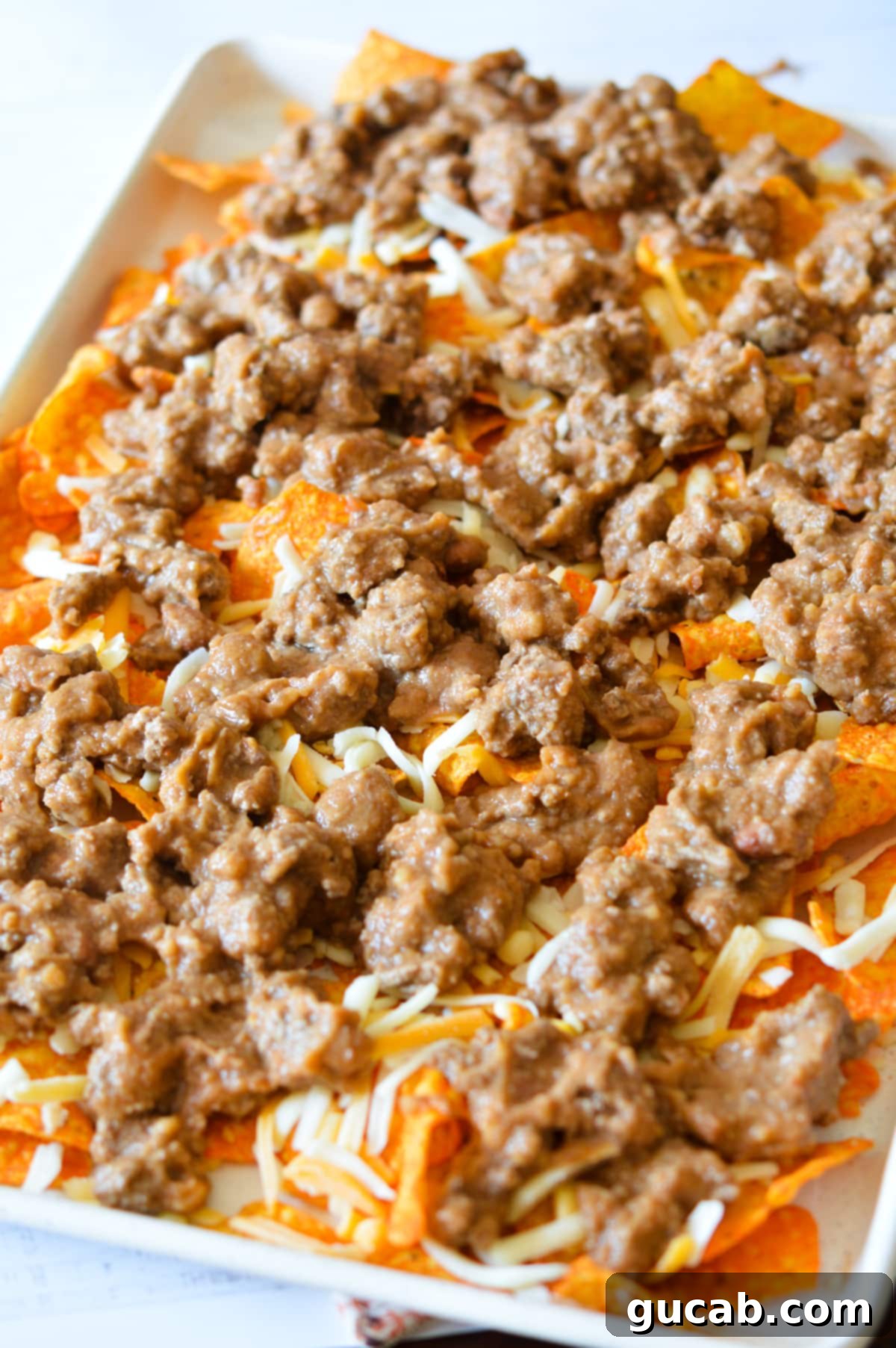Baked Doritos nachos on a sheet pan, with melted cheese, ground beef, and refried beans.