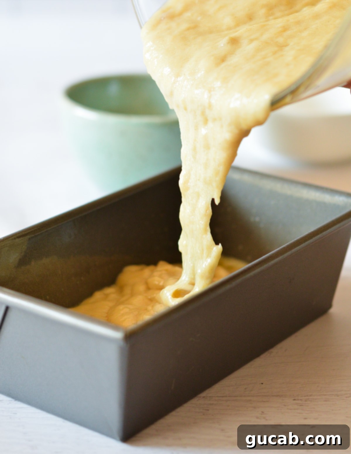 Thick banana bread batter being poured smoothly into a well-greased loaf pan, ready for baking.