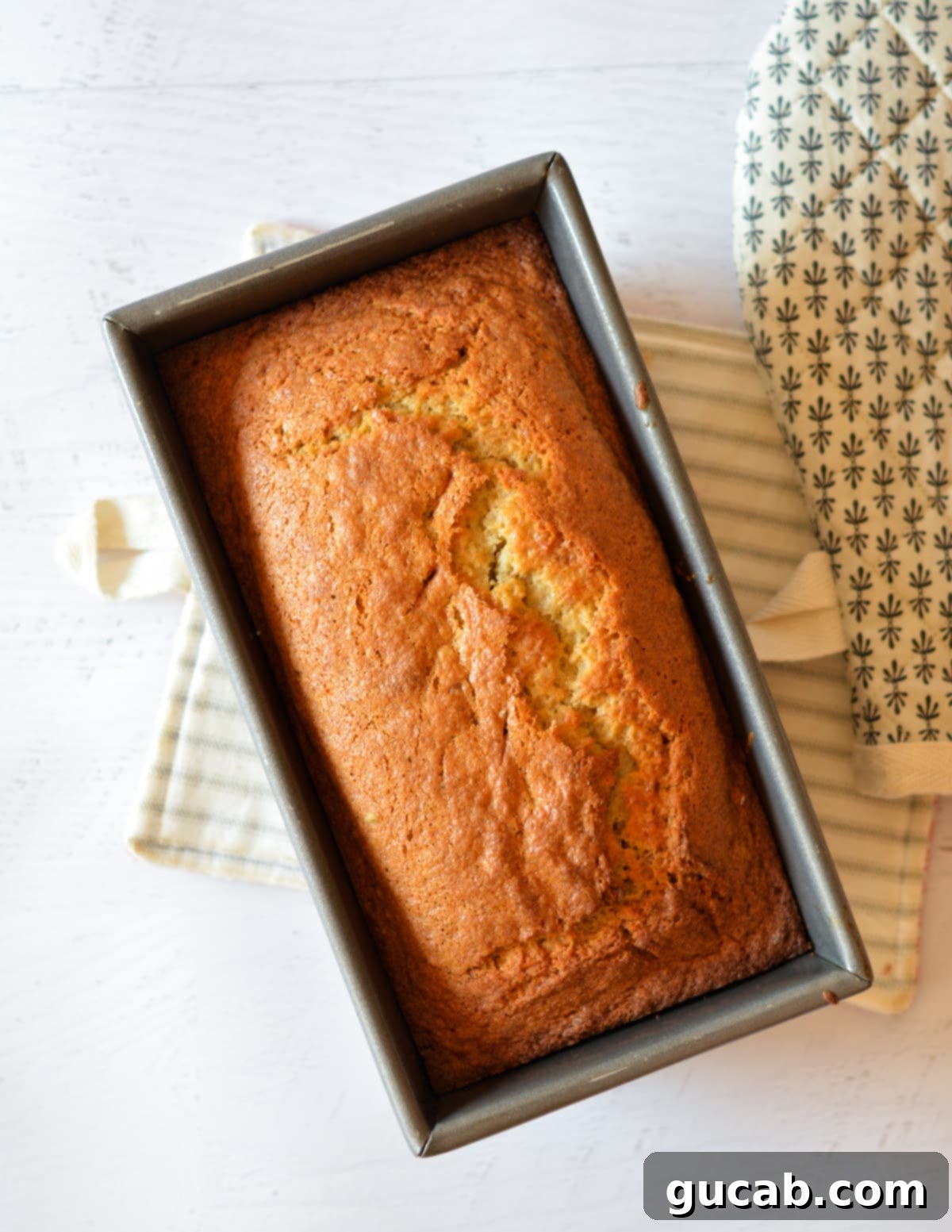 A freshly baked loaf of golden-brown banana bread resting in its pan, just out of the oven.