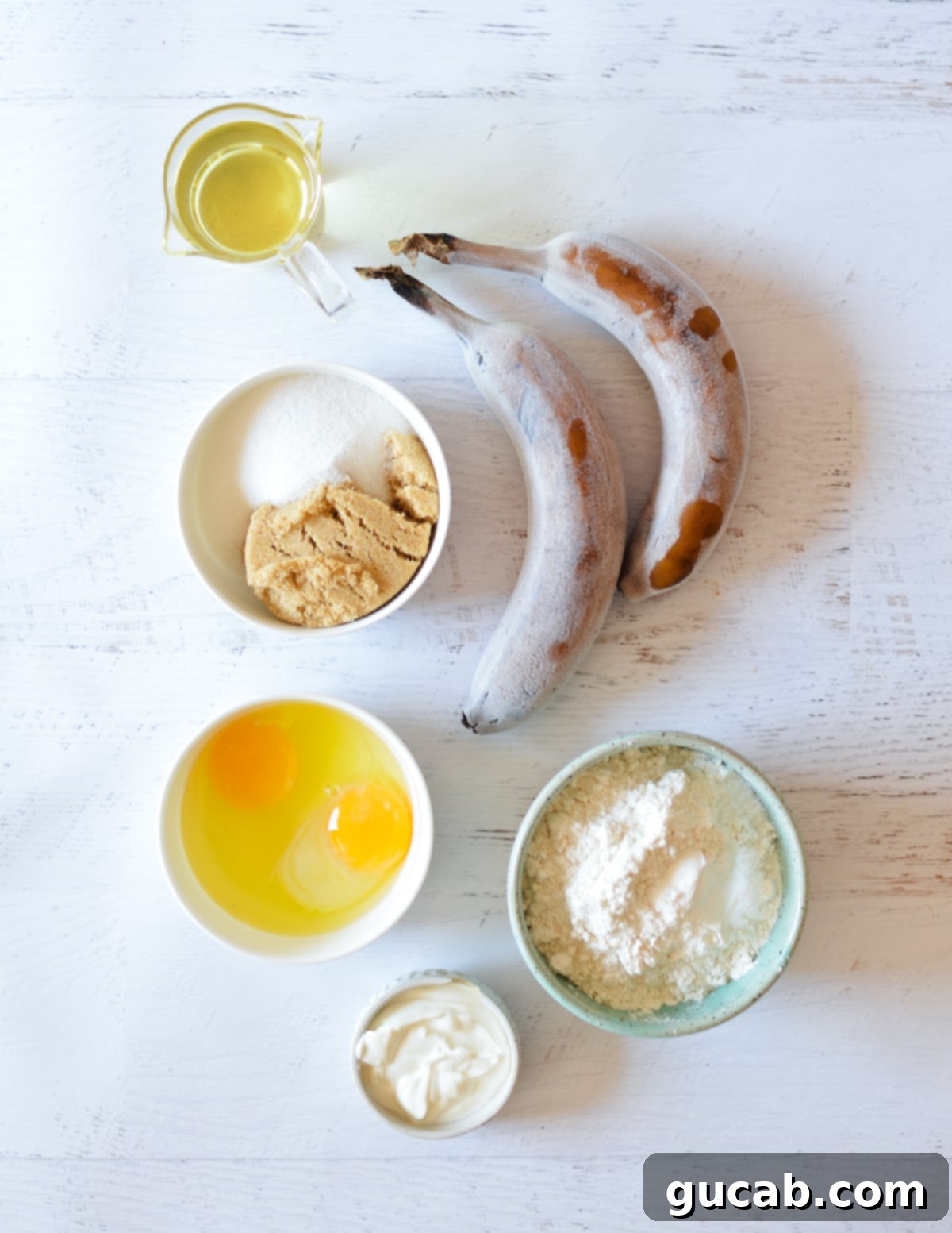 The Key to Amazing Banana Bread Frozen Bananas 3 A collection of banana bread ingredients: oil, frozen bananas, sugar, brown sugar, eggs, and flour, arranged neatly for a visual guide.