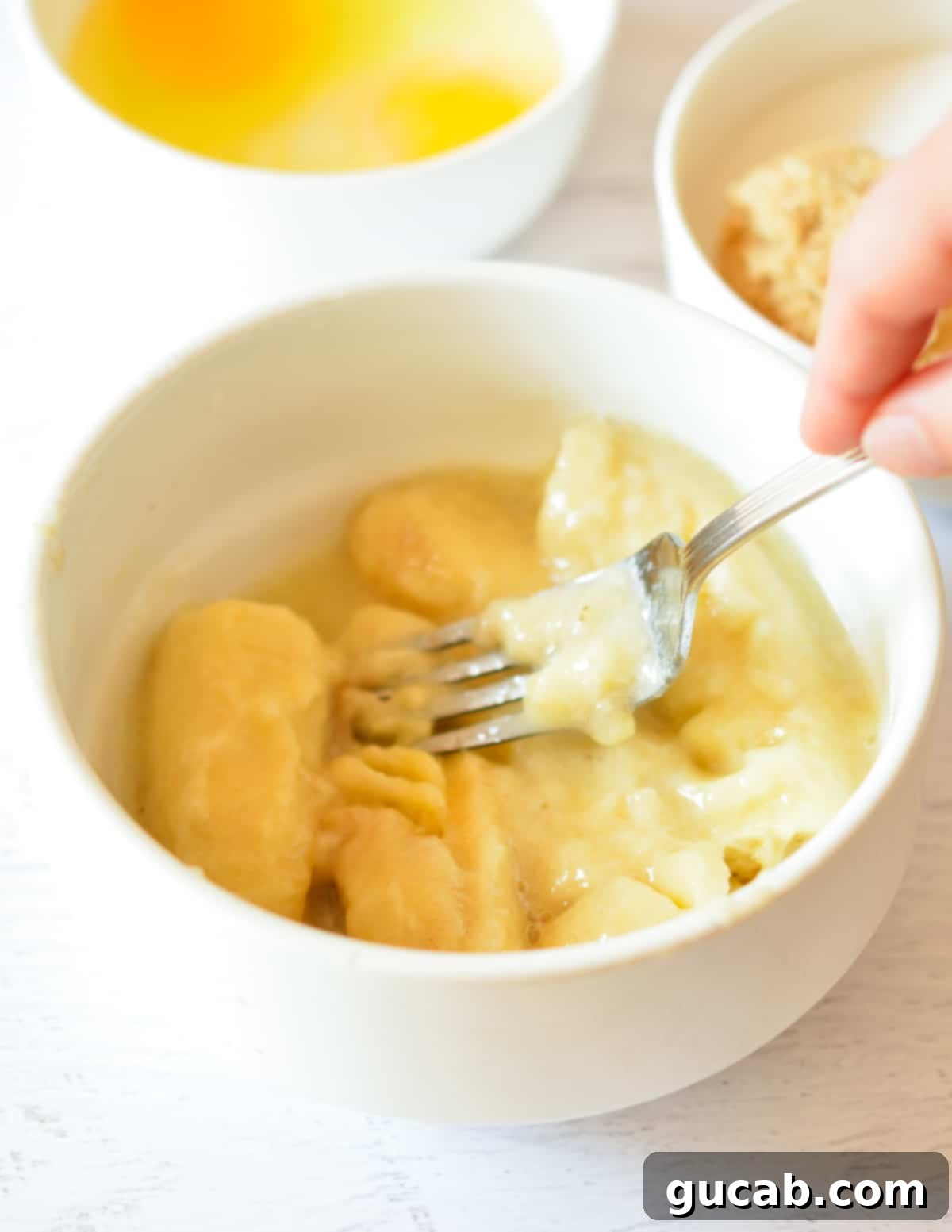 A fork actively mashing soft, thawed bananas in a bowl, preparing them for the batter.