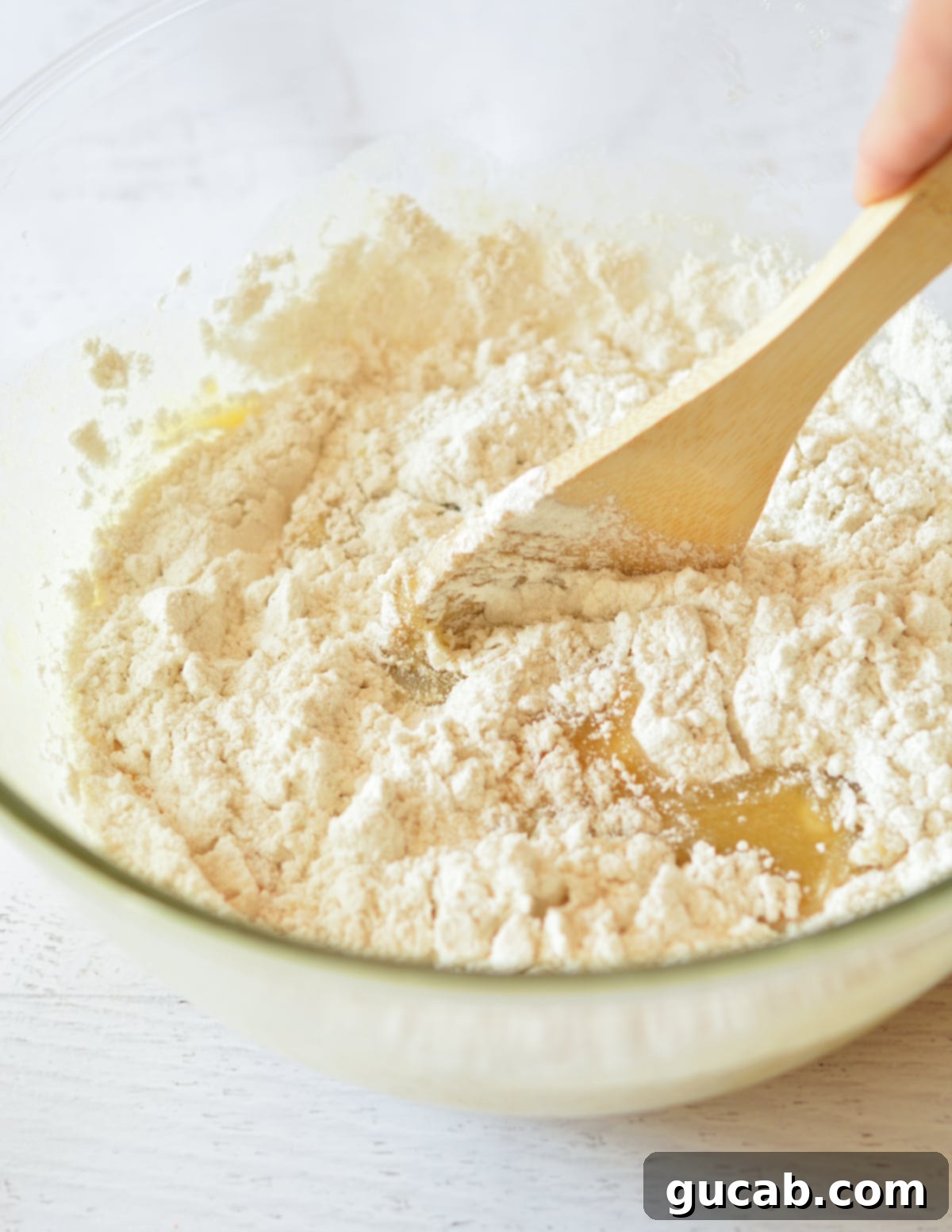 A hand stirring flour and mashed banana mixture together in a large bowl, forming the bread batter.