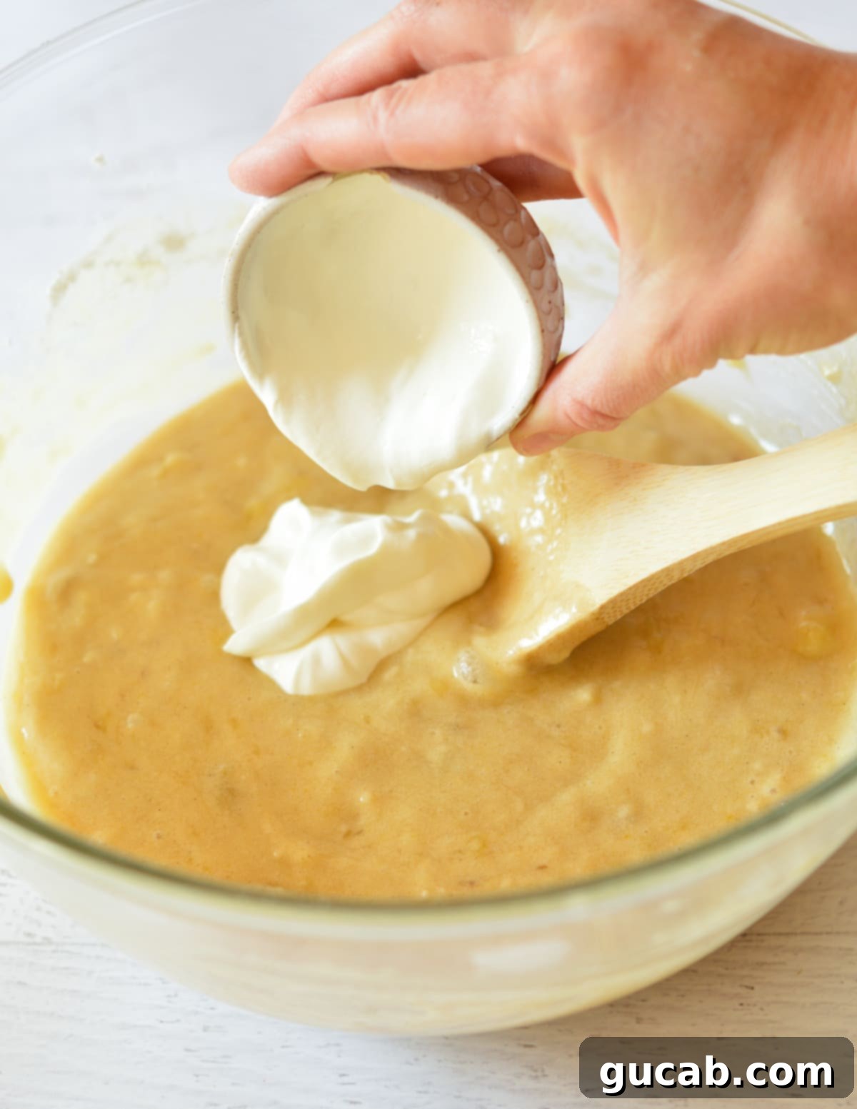 Sour cream being carefully poured into a bowl of banana bread batter, ready for its final mix.