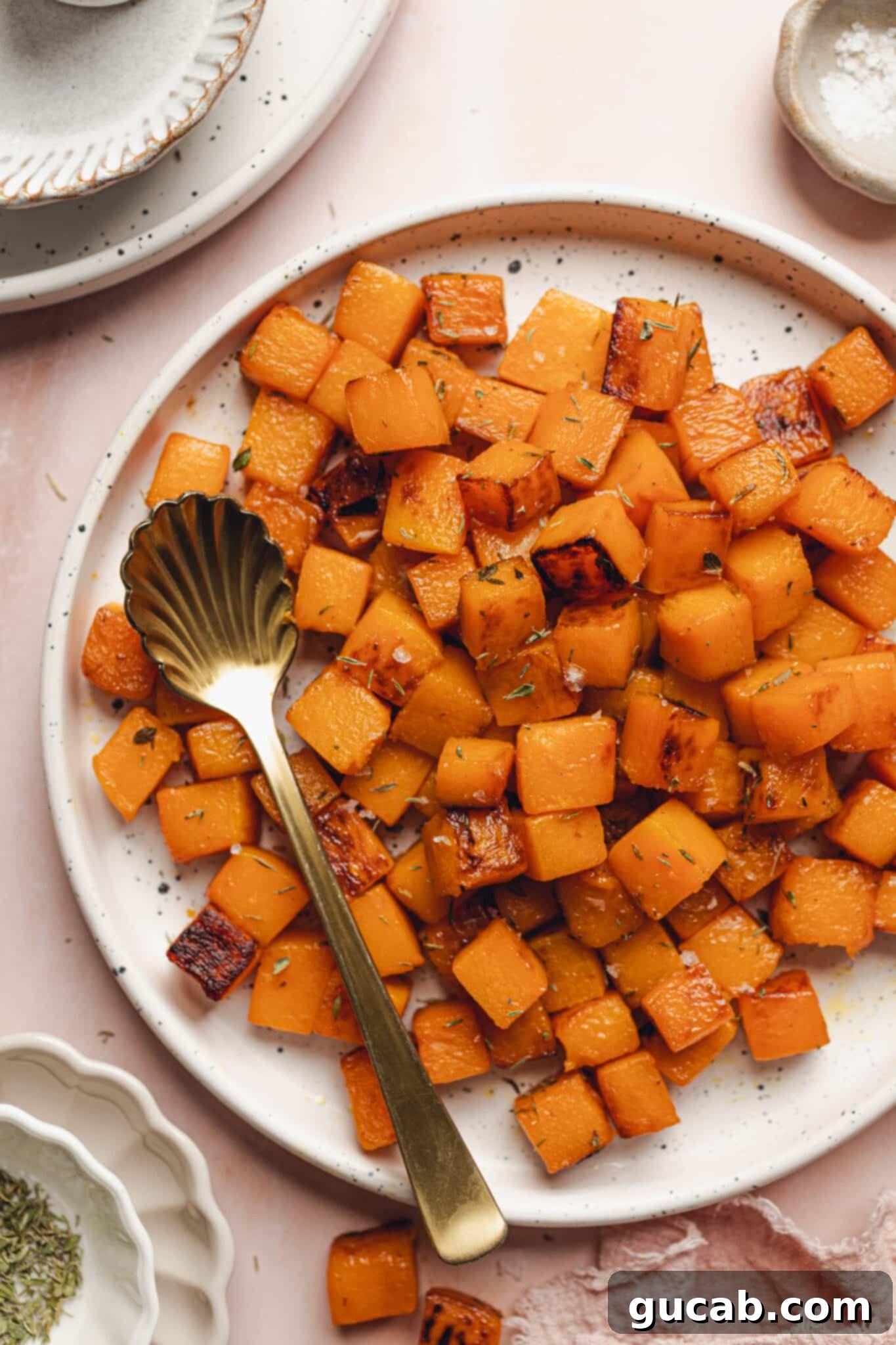 A plate of perfectly caramelized butternut squash cubes, garnished with a sprig of fresh thyme, showcasing its golden-brown crust and tender interior.