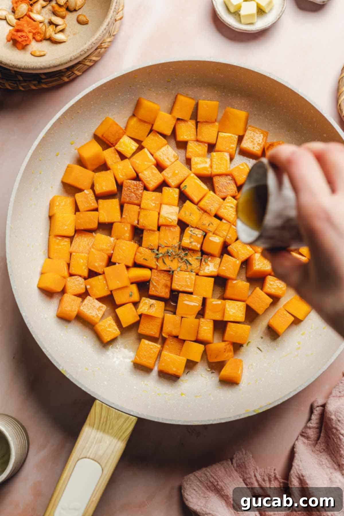Maple syrup being drizzled over sauteing butternut squash in a hot skillet, signaling the start of the glazing process.