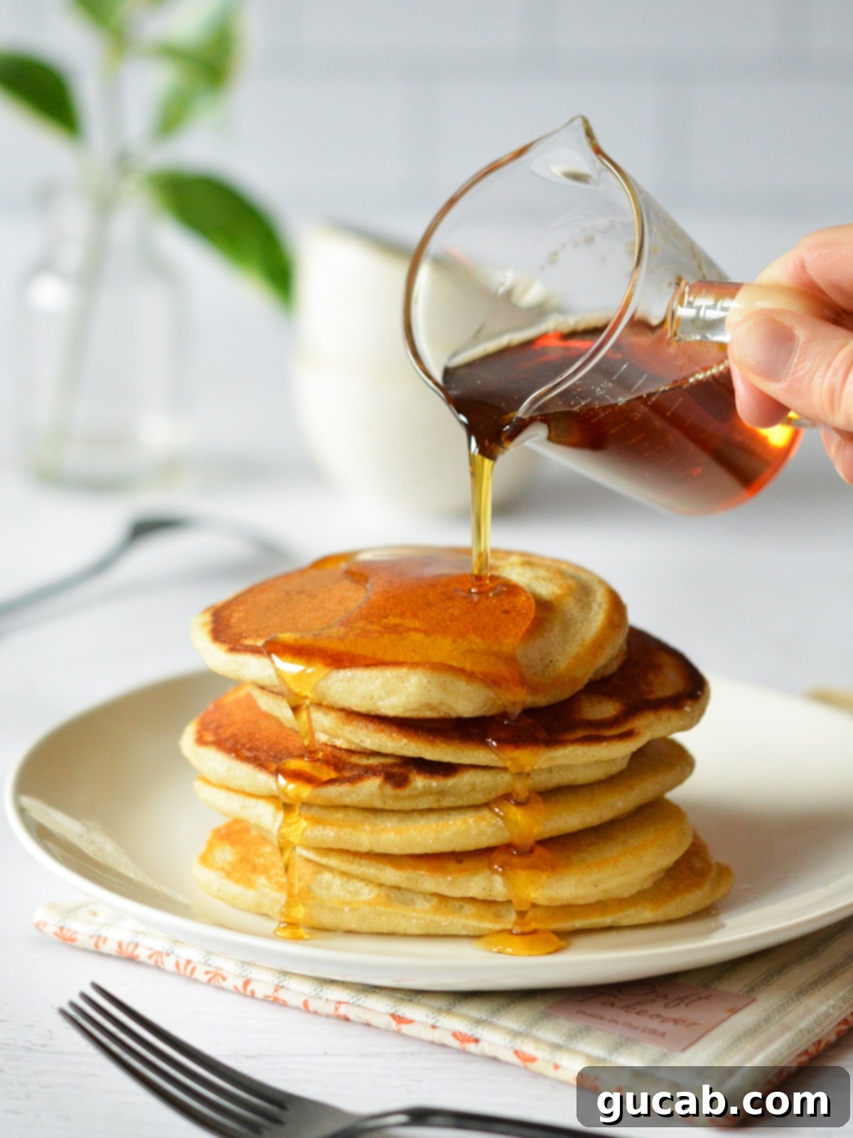 A stack of thin pancakes with crispy edges and maple syrup being drizzled on top, served on a plate.