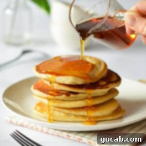 pouring maple syrup onto a stack of crispy pancakes.