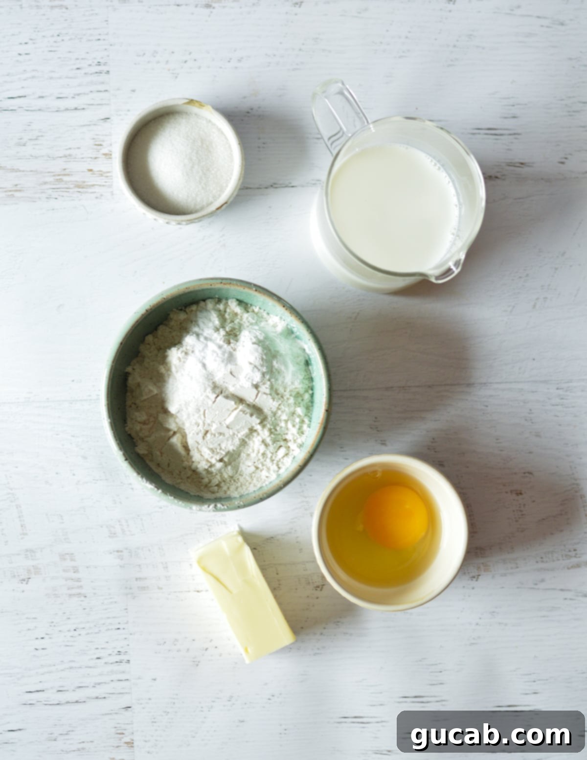 An arrangement of key pancake ingredients: granulated sugar, whole milk, all-purpose flour, large eggs, and melted unsalted butter.