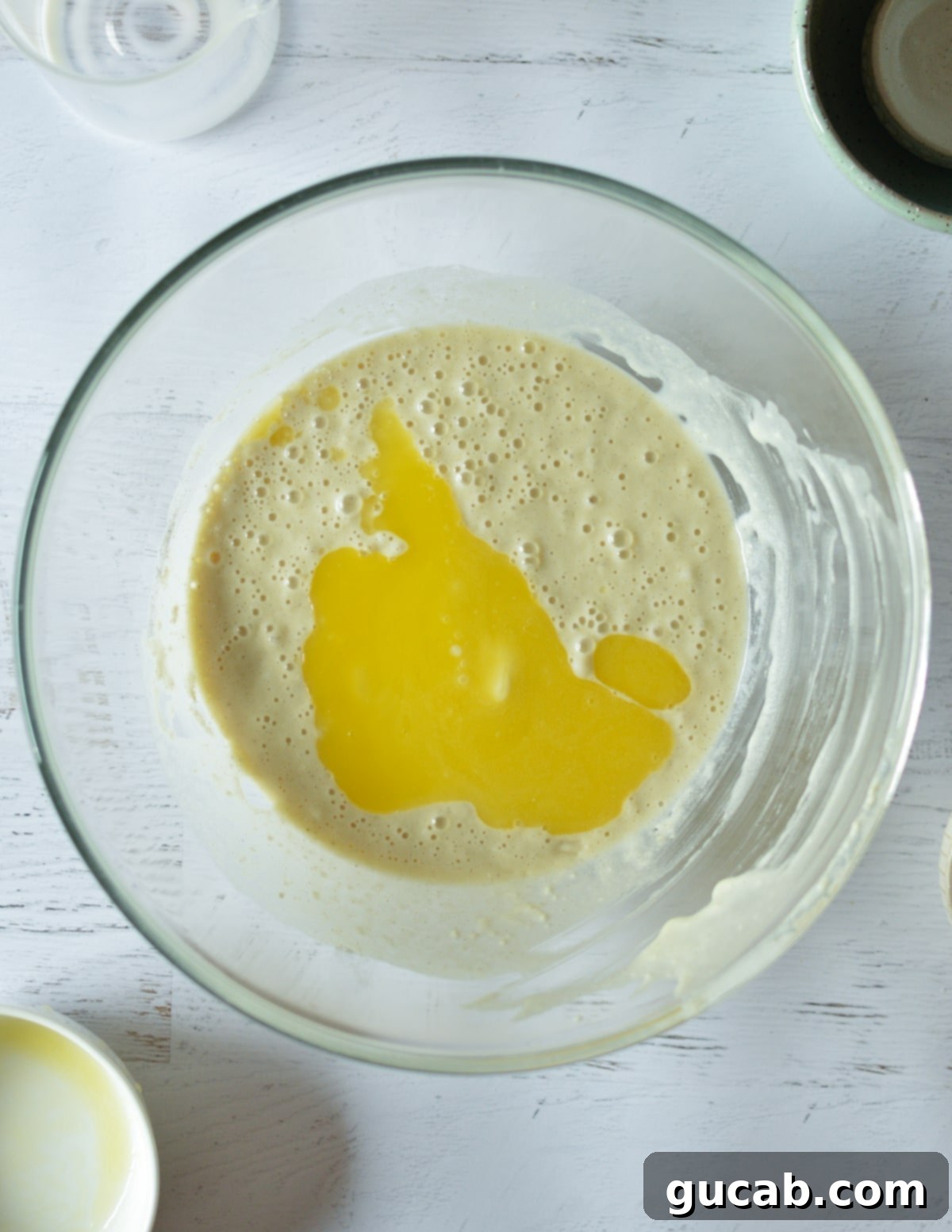 Pancake batter in a bowl with melted unsalted butter being added on top.
