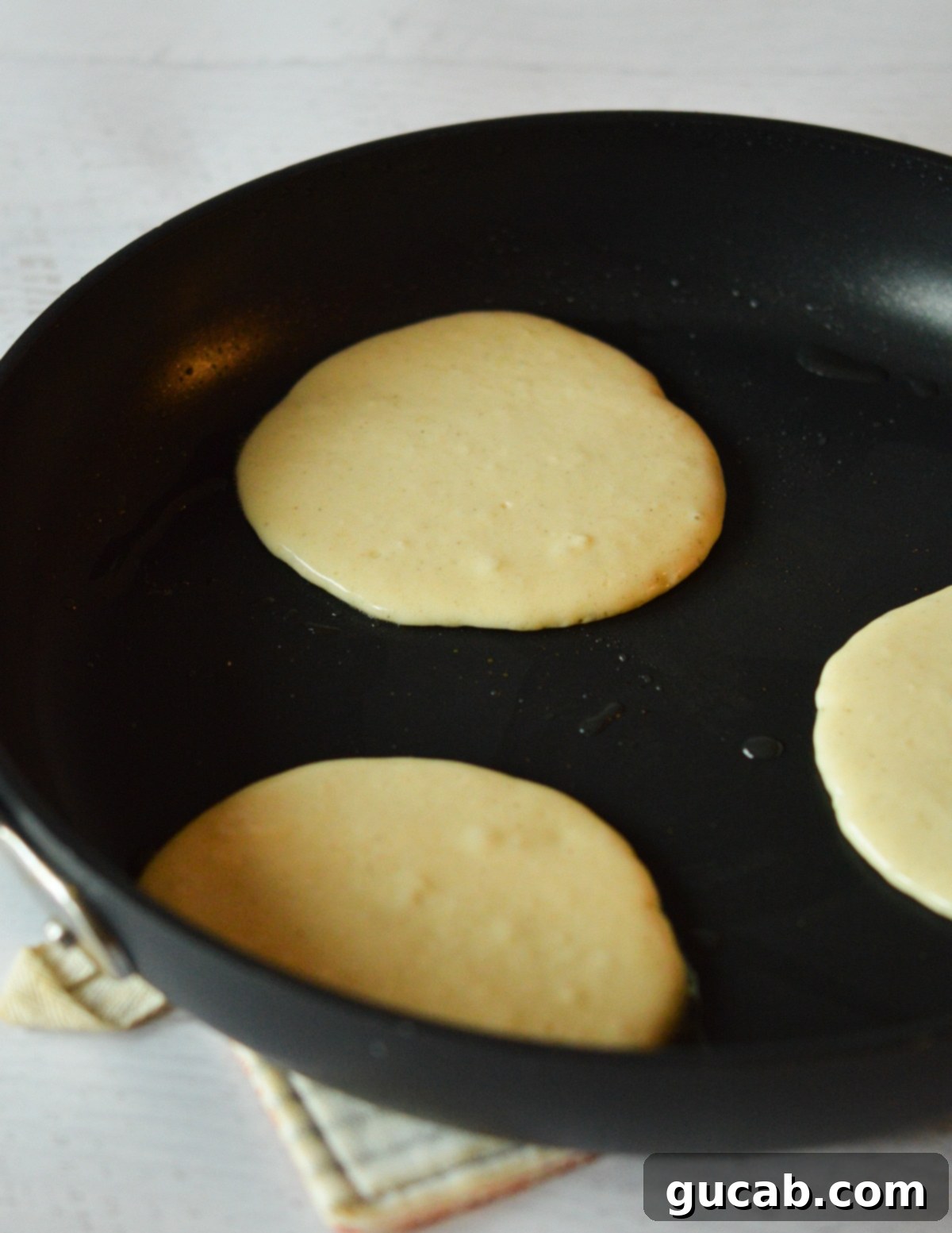 Pancake batter carefully dropped into a hot nonstick skillet, leaving space for spreading.