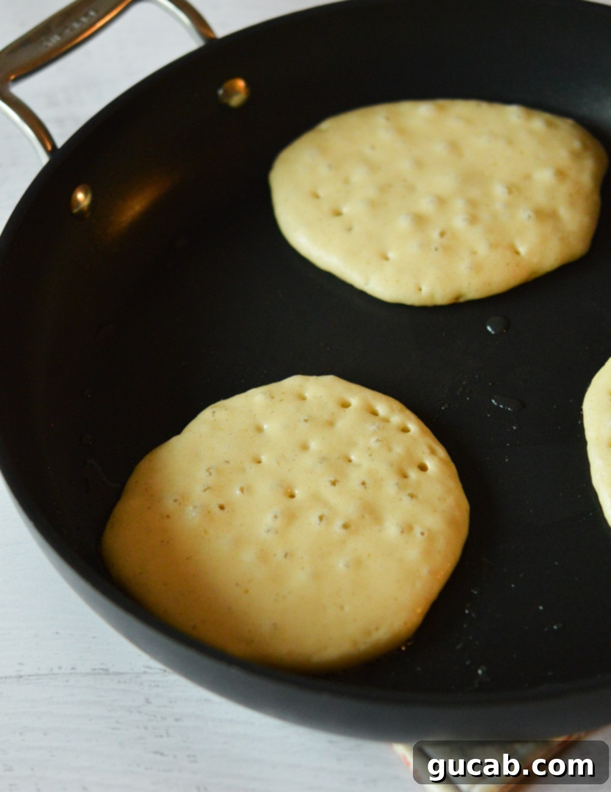 Pancake batter cooking in a skillet, showing visible bubbles on the surface, indicating it's almost ready to flip.