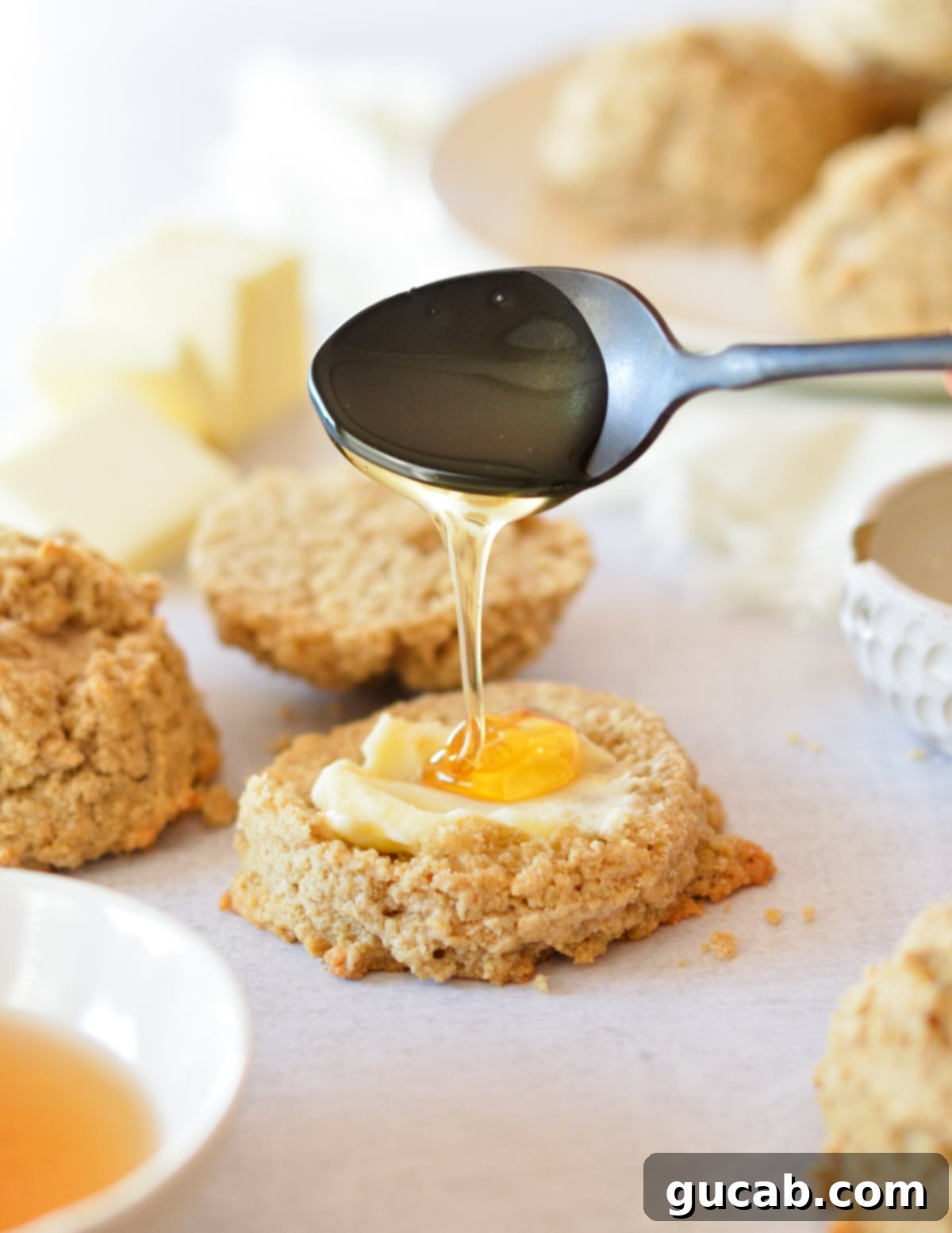 Honey being drizzled onto a freshly baked, buttered oat flour biscuit, highlighting its light texture.