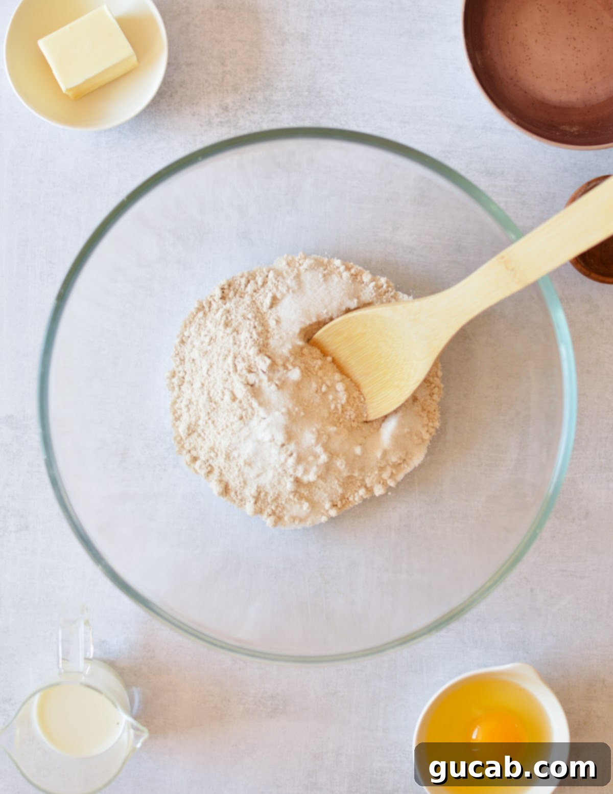 A large wooden spoon rests inside a bowl filled with finely ground oat flour, mixed with other dry ingredients.