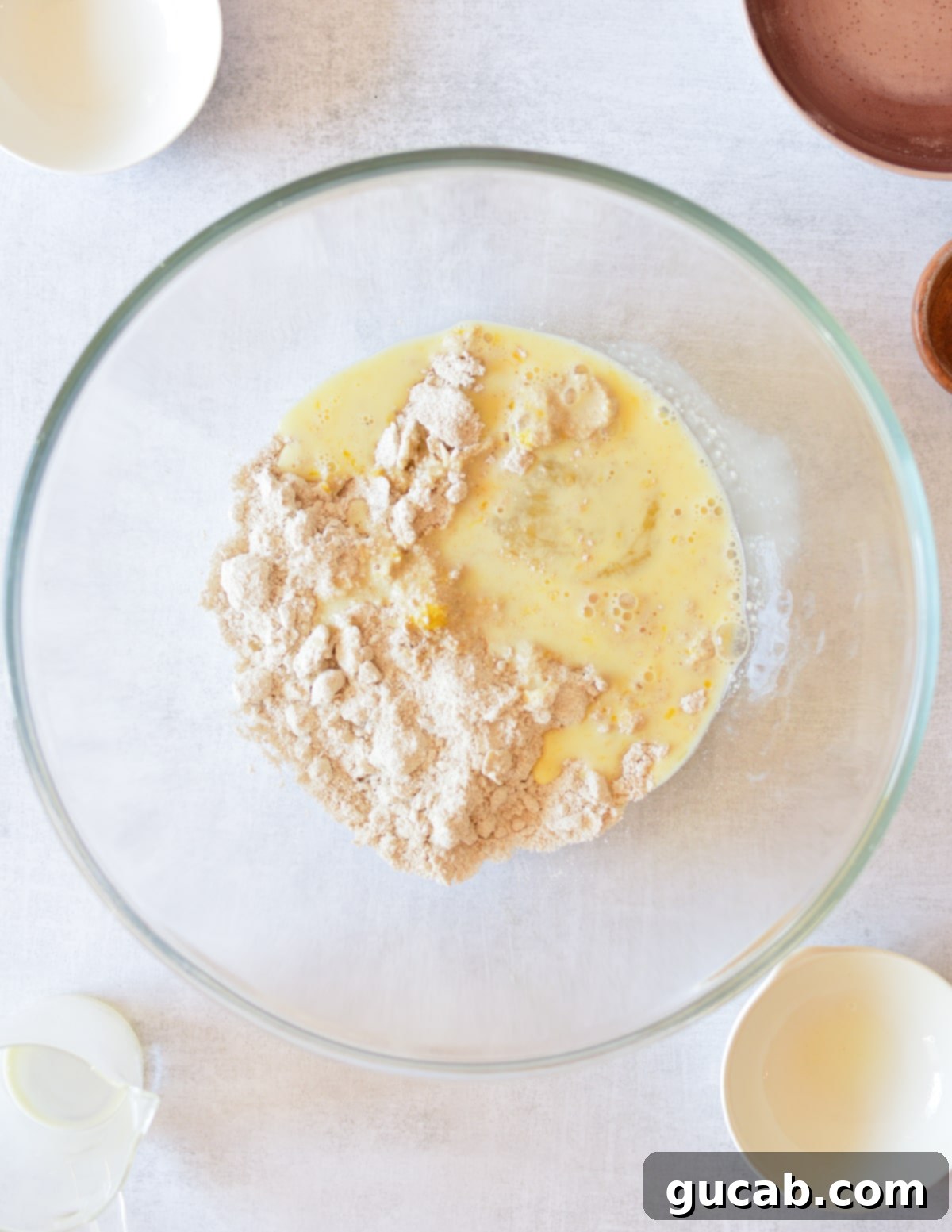The wet milk and egg mixture has just been poured over the oat flour and butter in a bowl, ready for gentle mixing.