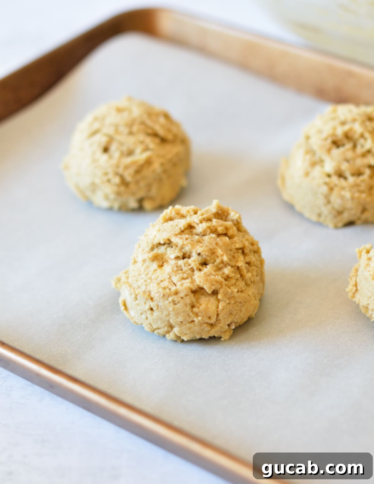 Four unbaked oat flour drop biscuits neatly scooped onto a parchment-lined baking sheet, ready for the oven.