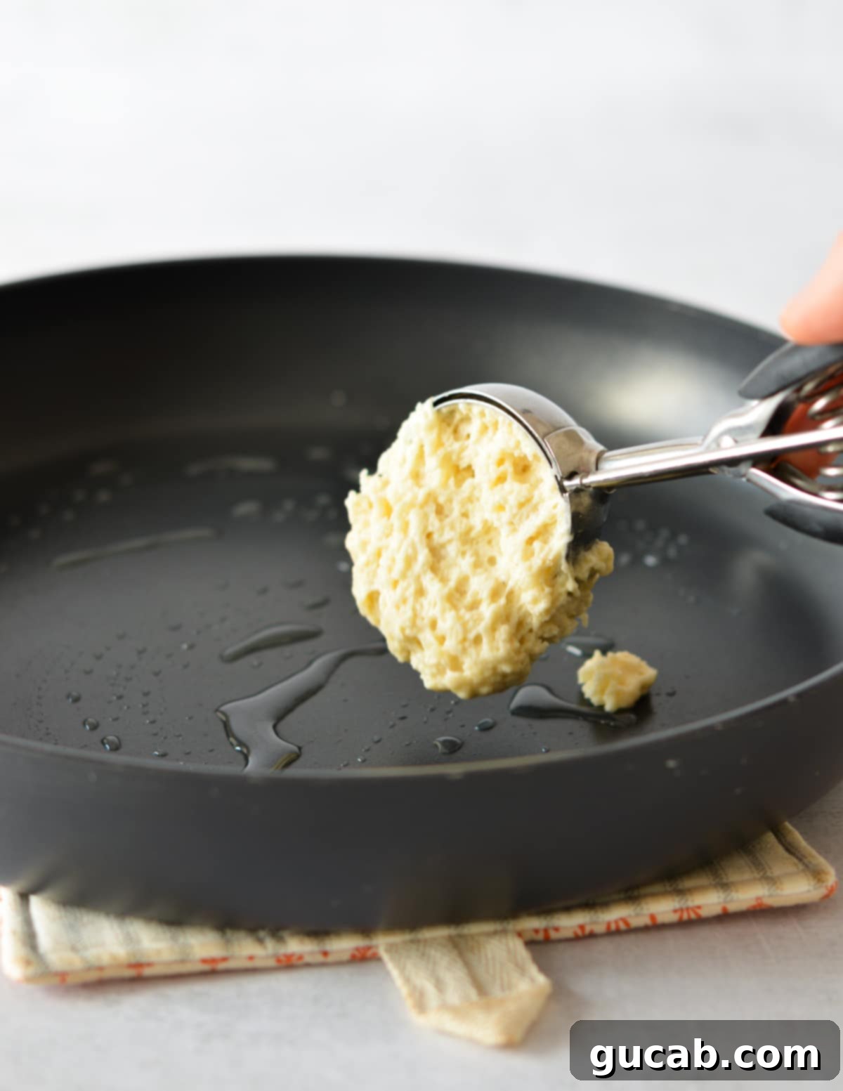 Fluffy Honey Pancakes 7 a scoop of pancake batter falling into a hot skillet with oil.