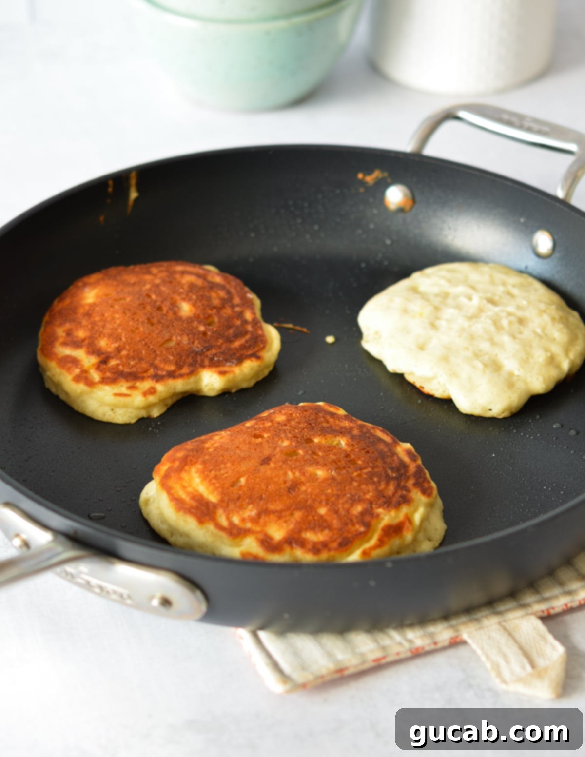 Fluffy Honey Pancakes 9 golden brown pancakes in a skillet with one pancake not flipped yet.