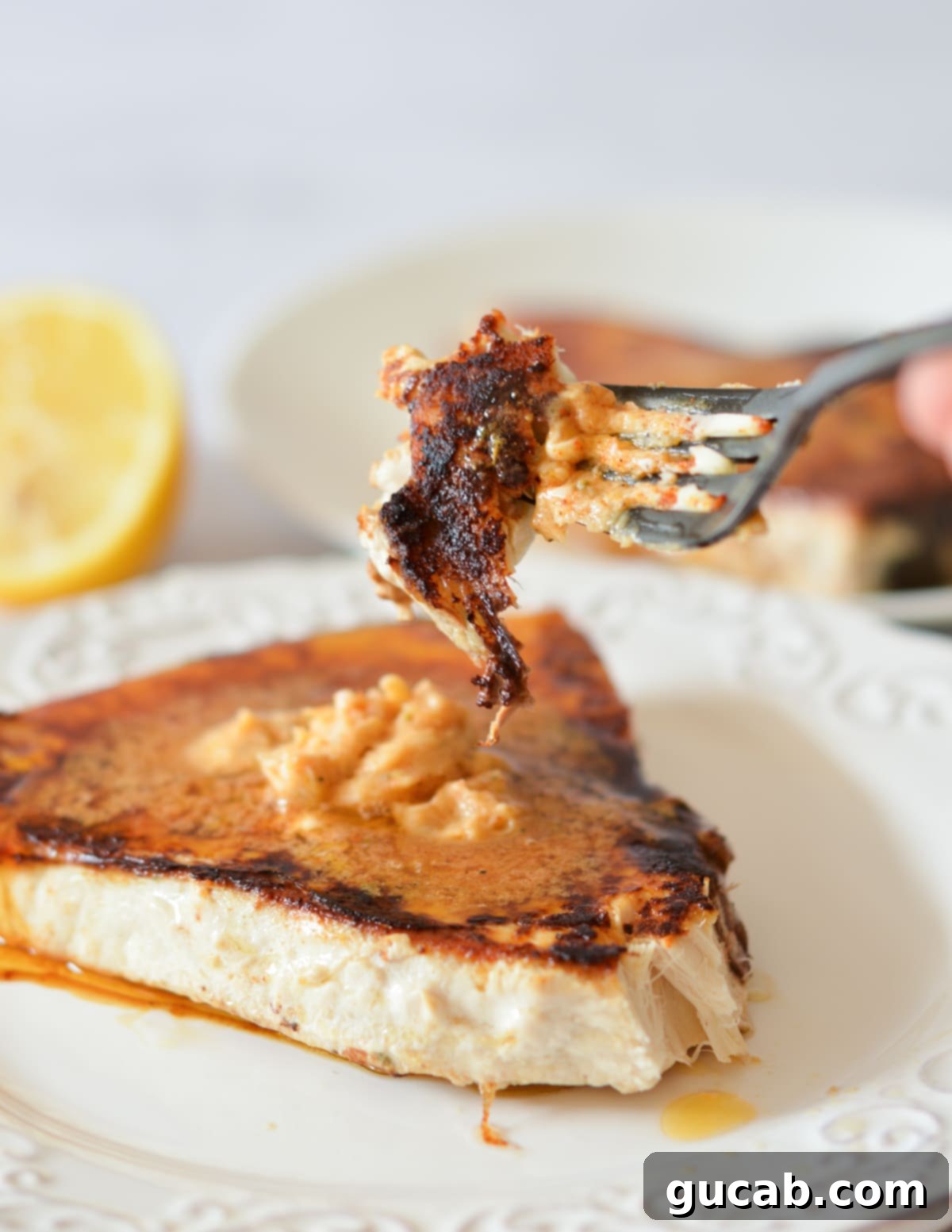 A fork taking a bite of blackened swordfish, showing the flaky texture and melted Cajun butter.