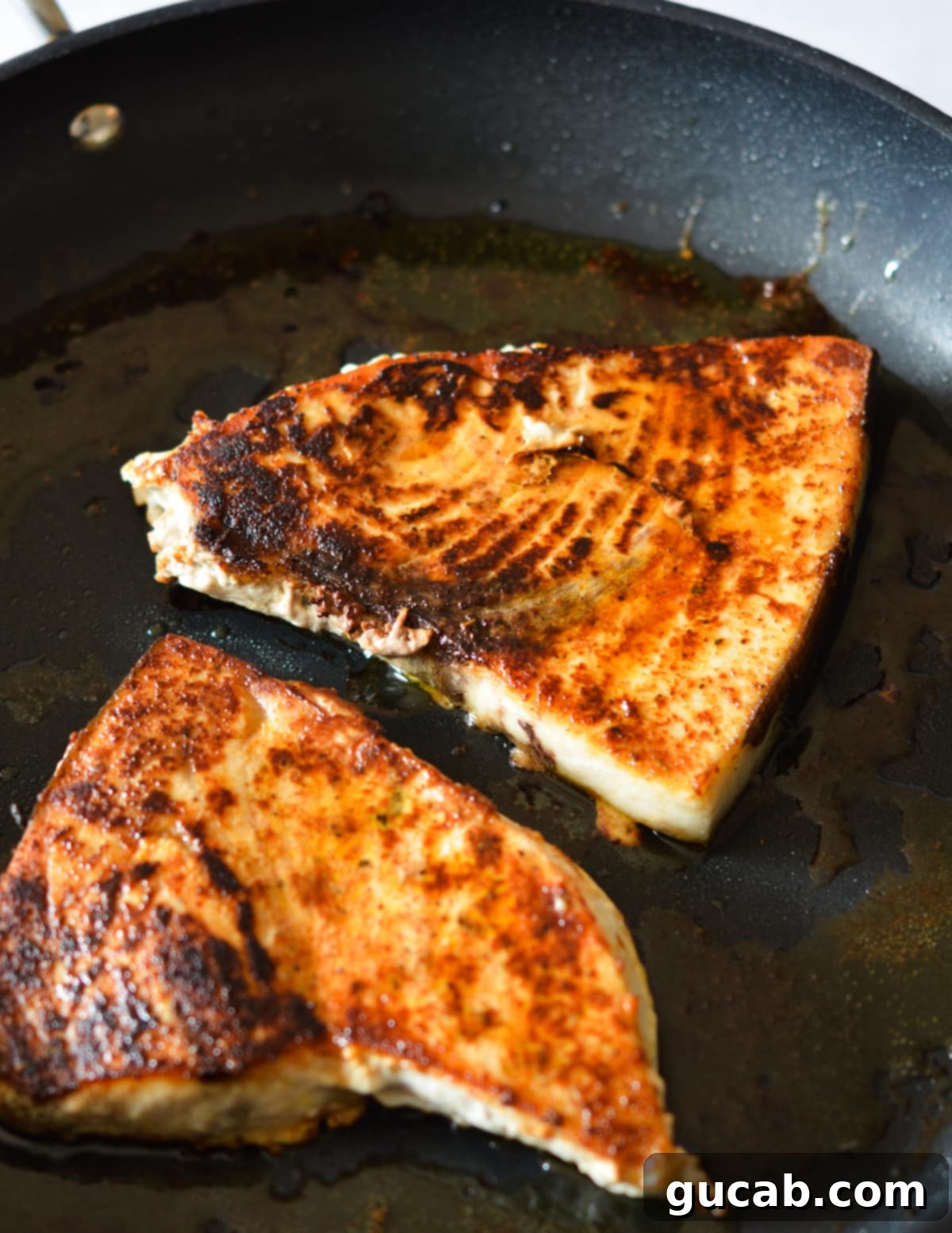 Two perfectly cooked blackened swordfish steaks in a skillet with residual olive oil, ready to be served.