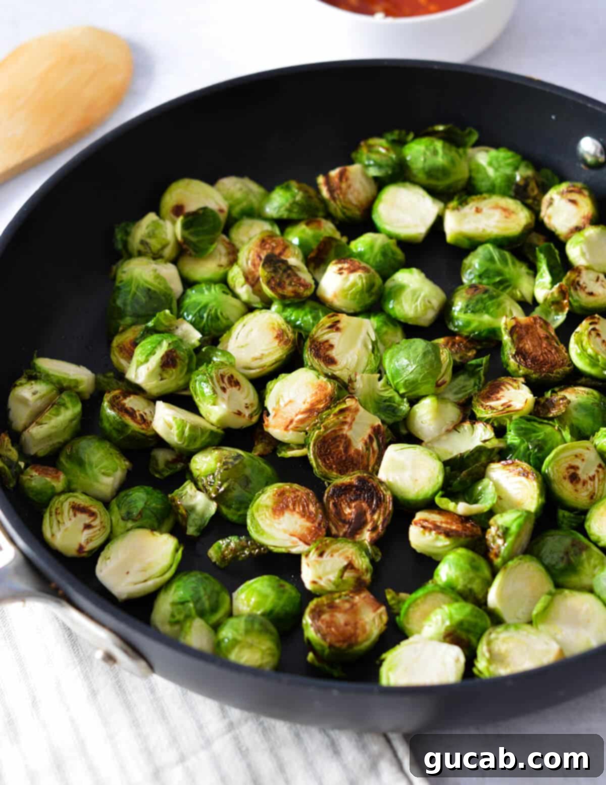 A close-up view of brussels sprouts getting tossed and coated in the sticky honey sriracha glaze in a skillet.