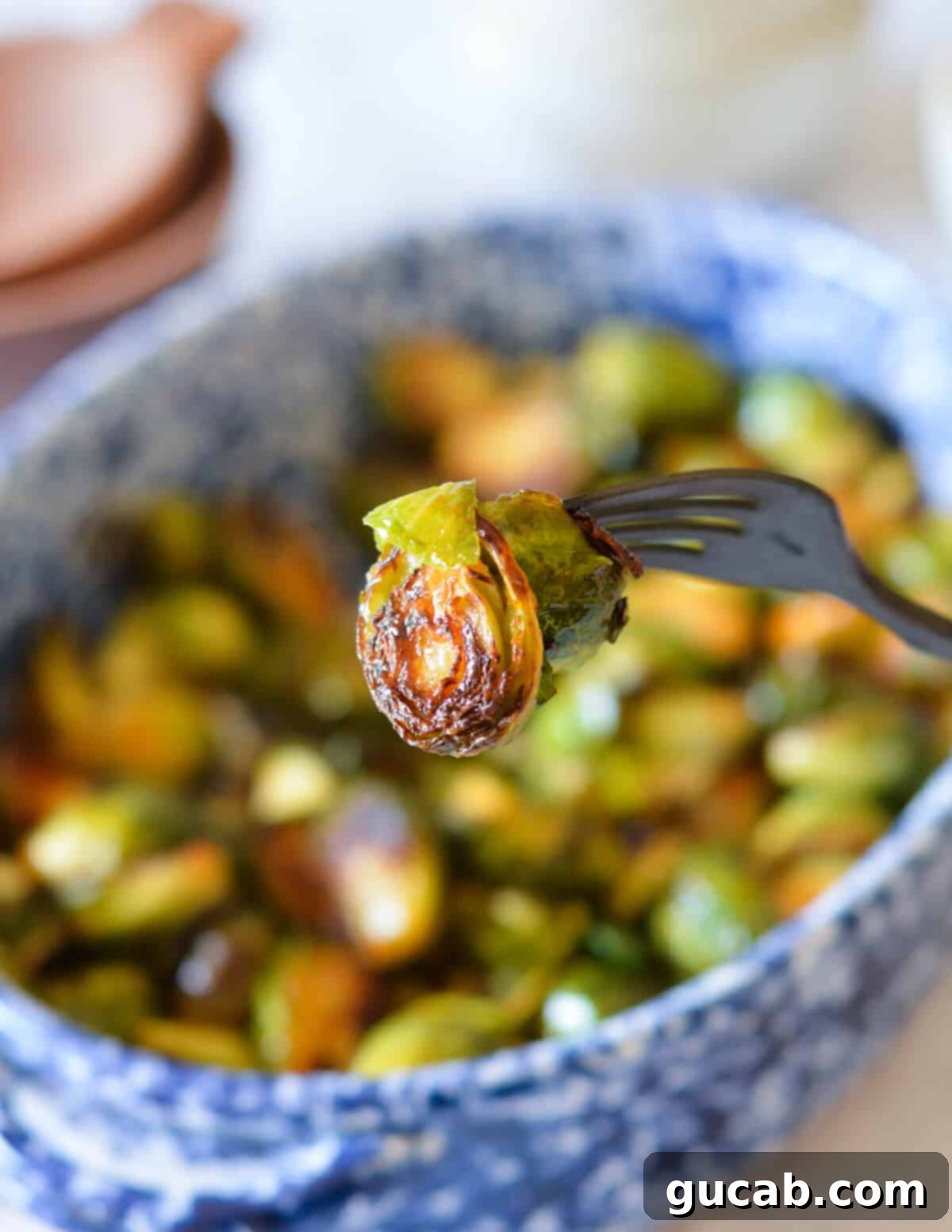 A fork piercing a single, perfectly glazed honey sriracha brussels sprout, ready to be enjoyed.