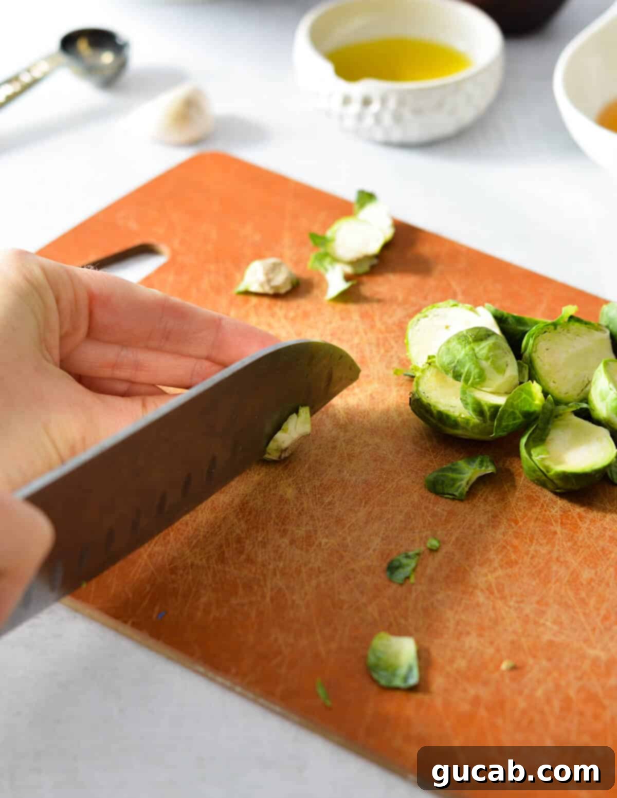 A hand carefully cutting the tough end off a fresh brussels sprout.