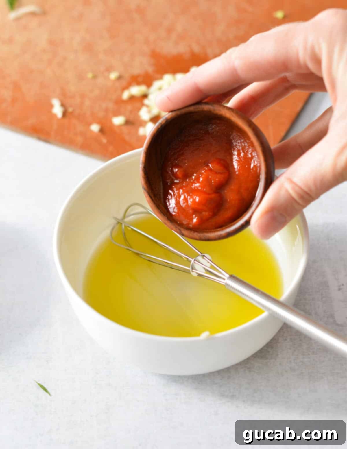 A stream of sriracha sauce being poured into a bowl containing olive oil, a crucial step in preparing the spicy honey glaze.