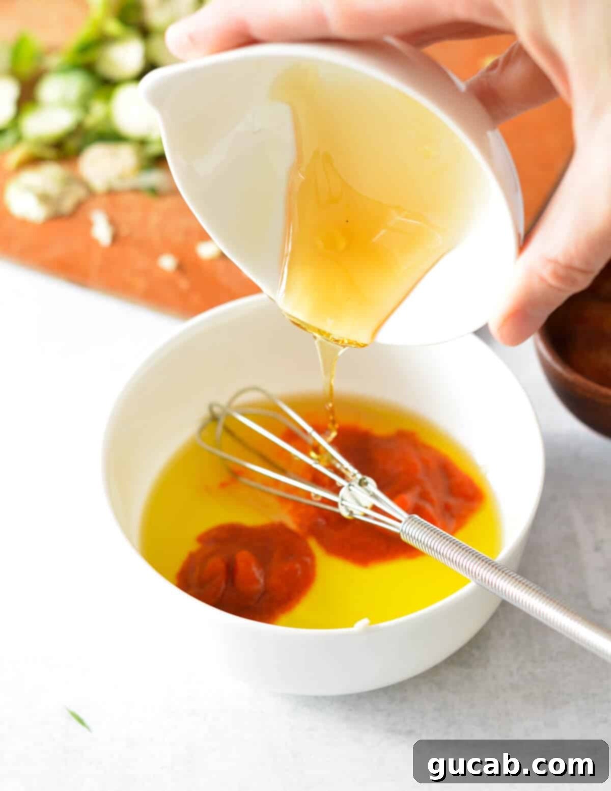 Golden honey drizzling into a bowl already holding olive oil and sriracha, forming the base of the sweet and spicy sauce.